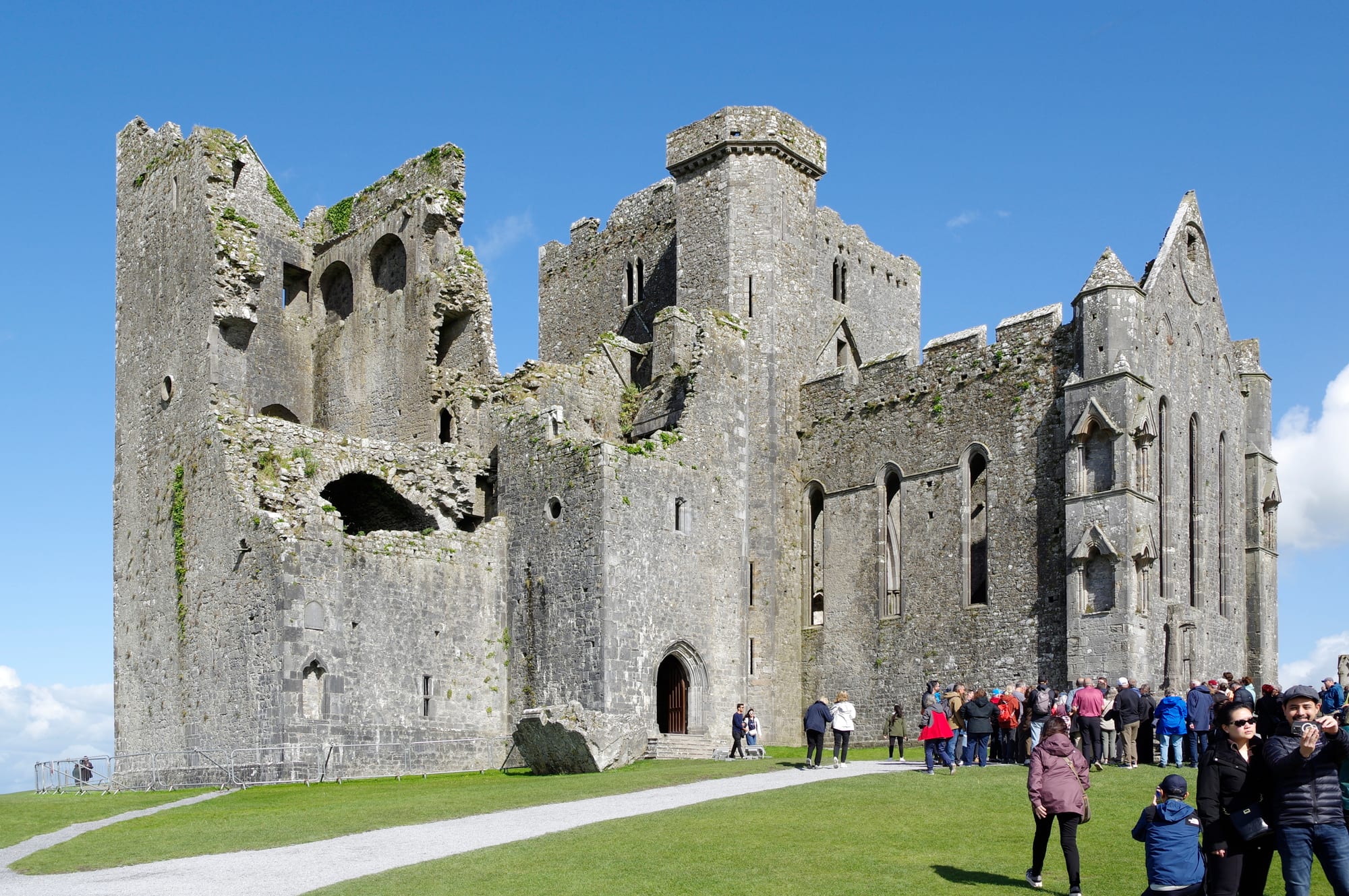 A cluster of medieval stone towers, a chapel, and a cathedral ruin on a grassy limestone outcrop