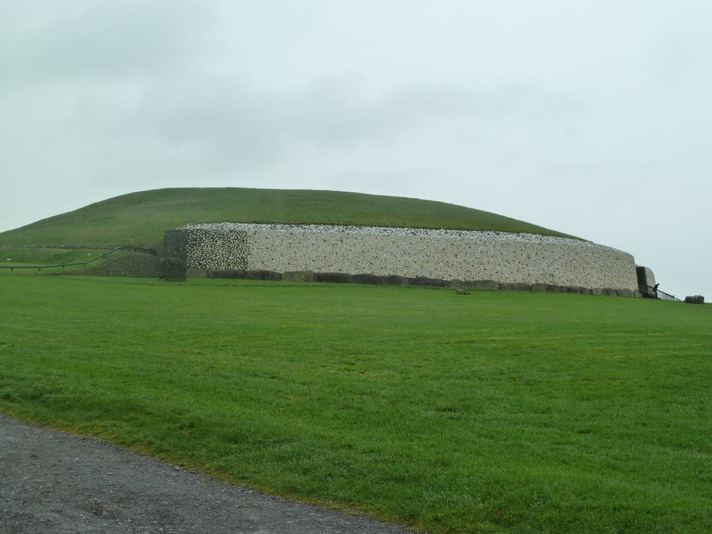 A large grass-topped circular mound faced with white quartz and grey stone, ringed by kerbstones