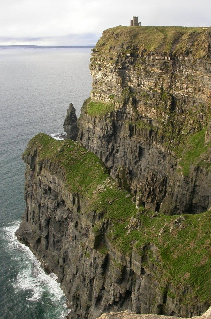 Sheer dark sea cliffs curving along a coastline, a lone tower on the highest point, ocean below