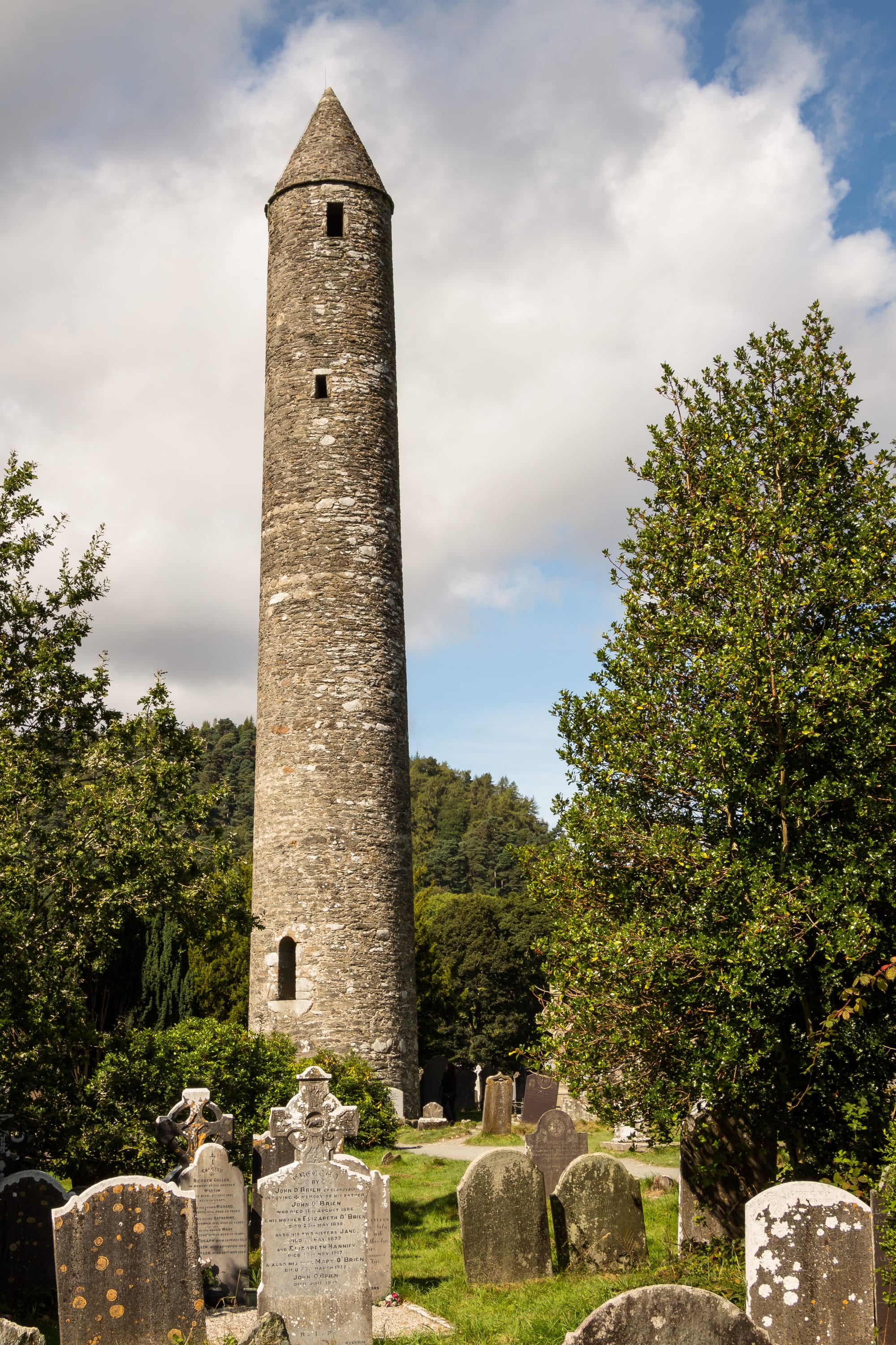 A round tower and stone church ruins beside a dark lake in a wooded glacial valley