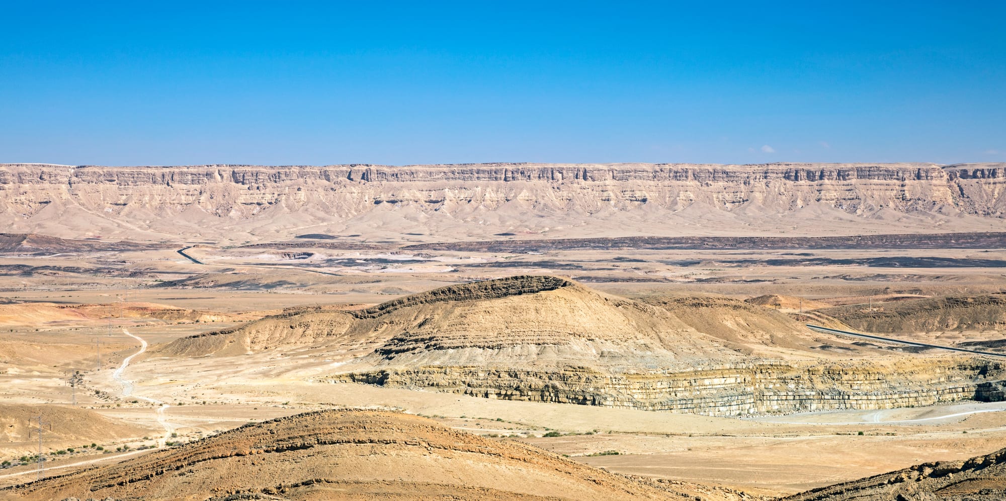 A vast eroded desert crater with layered rock walls and a flat, sparse floor