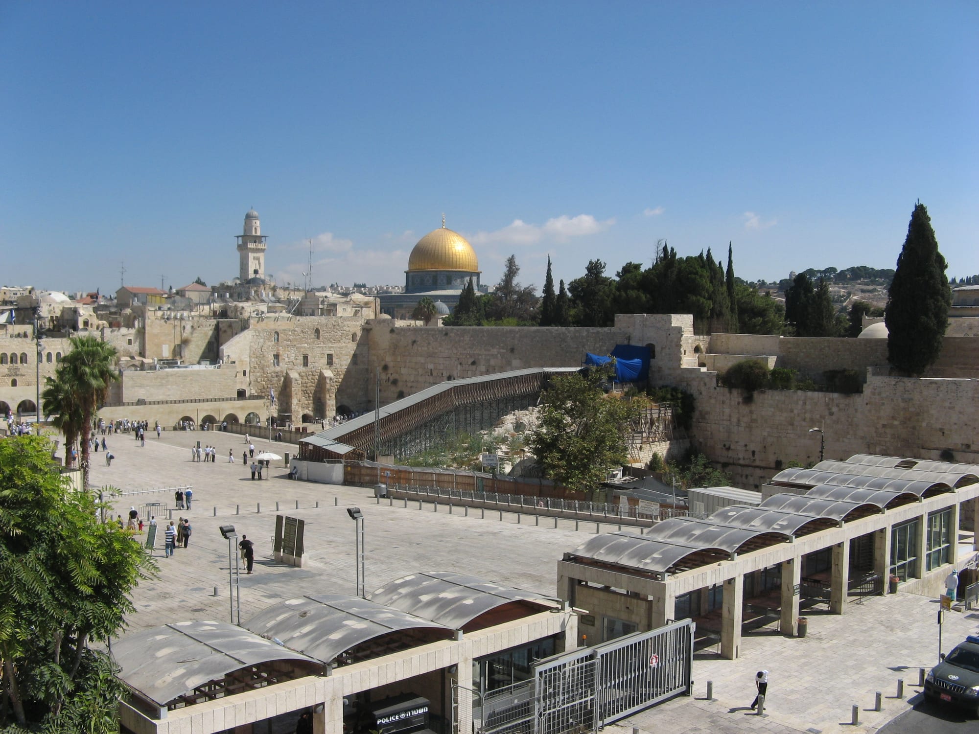 People praying at a huge ancient stone wall, a golden dome rising behind it