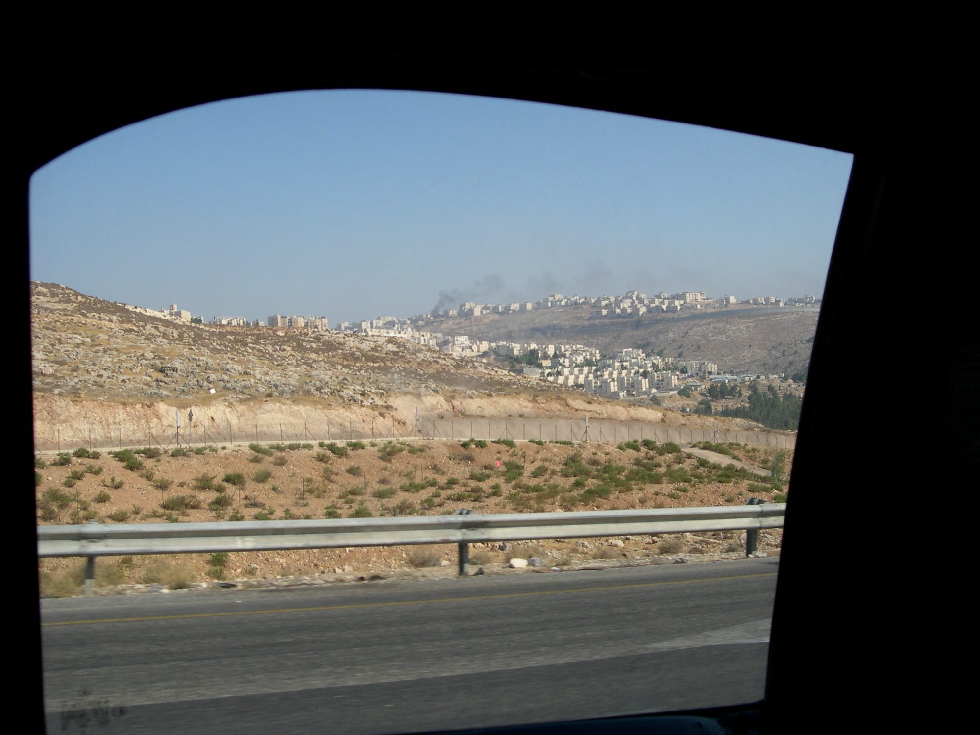Two hilltop Israeli settlements of red-roofed houses across a valley in the West Bank