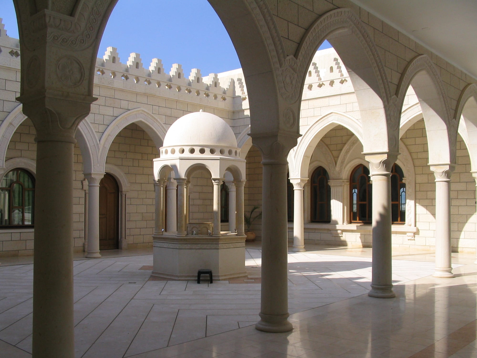 A pale stone courtyard seen through a row of arches, with a small domed fountain pavilion at its centre and tall arched windows beyond