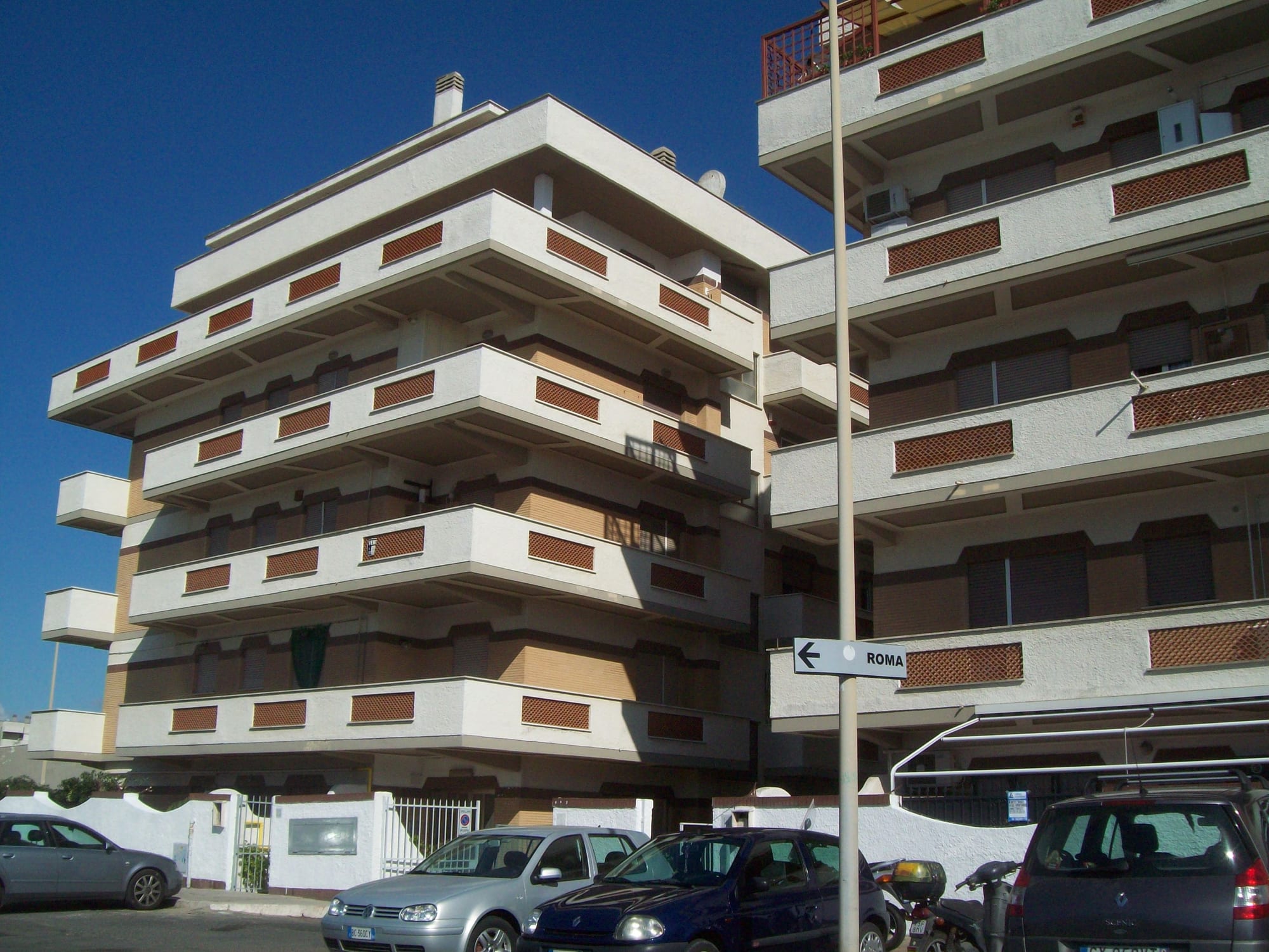 A multi-storey apartment building near Rome with stacked balconies and closed roller shutters on many windows