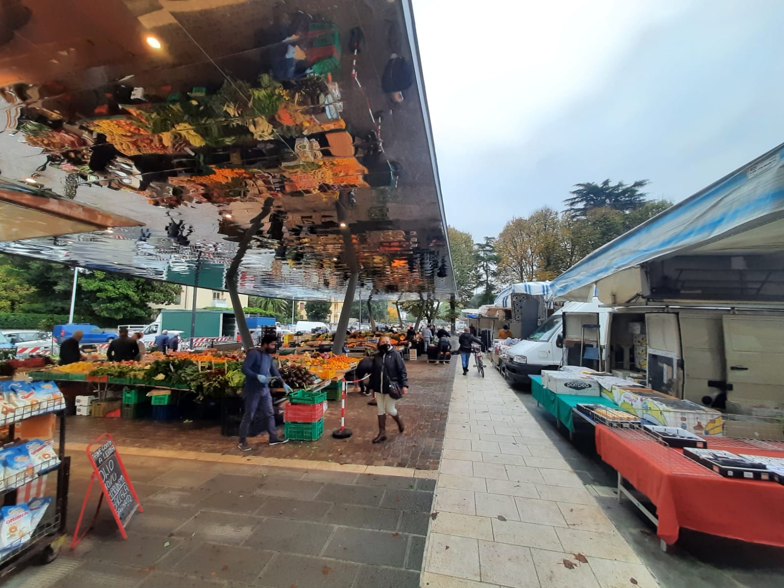 An open-air fruit and vegetable market under awnings in a Florence piazza, with vendors and shoppers among the stalls