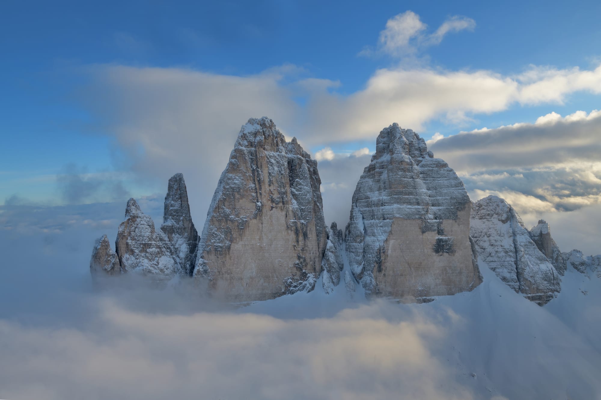 Three enormous vertical rock towers rising side by side above alpine meadow and scree