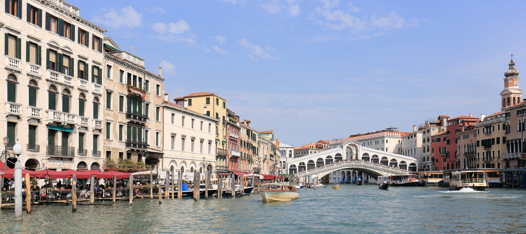 A wide curving canal lined with palaces, a white stone arched bridge crossing it, boats everywhere