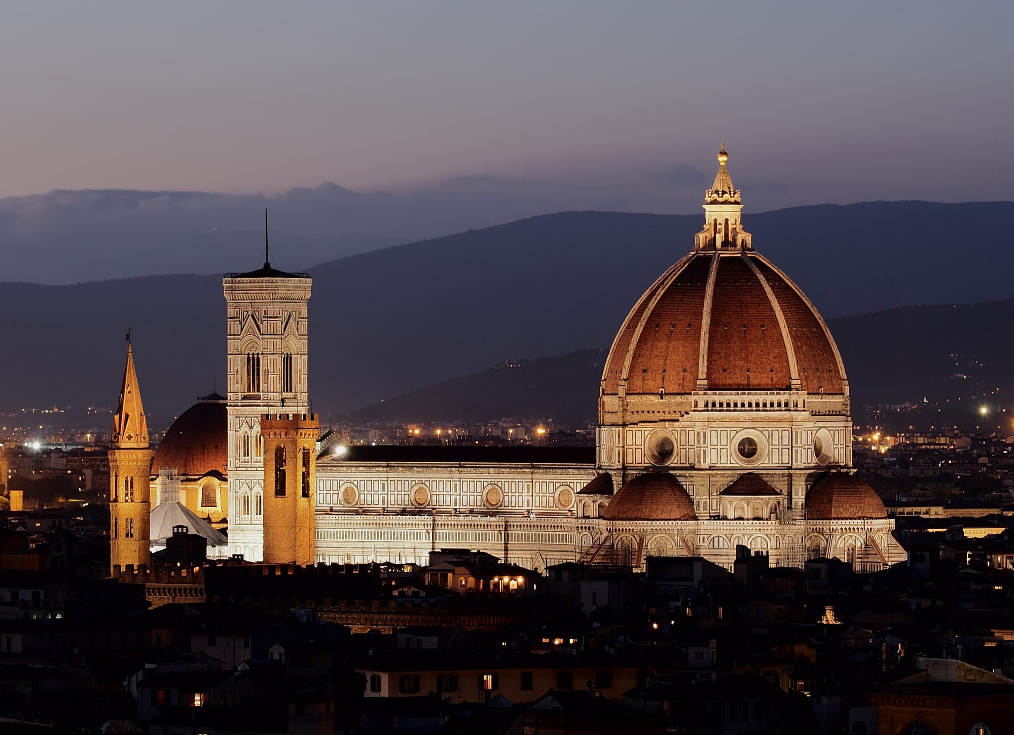 A red-tiled dome dominating a city of stone towers and rooftops, hills beyond