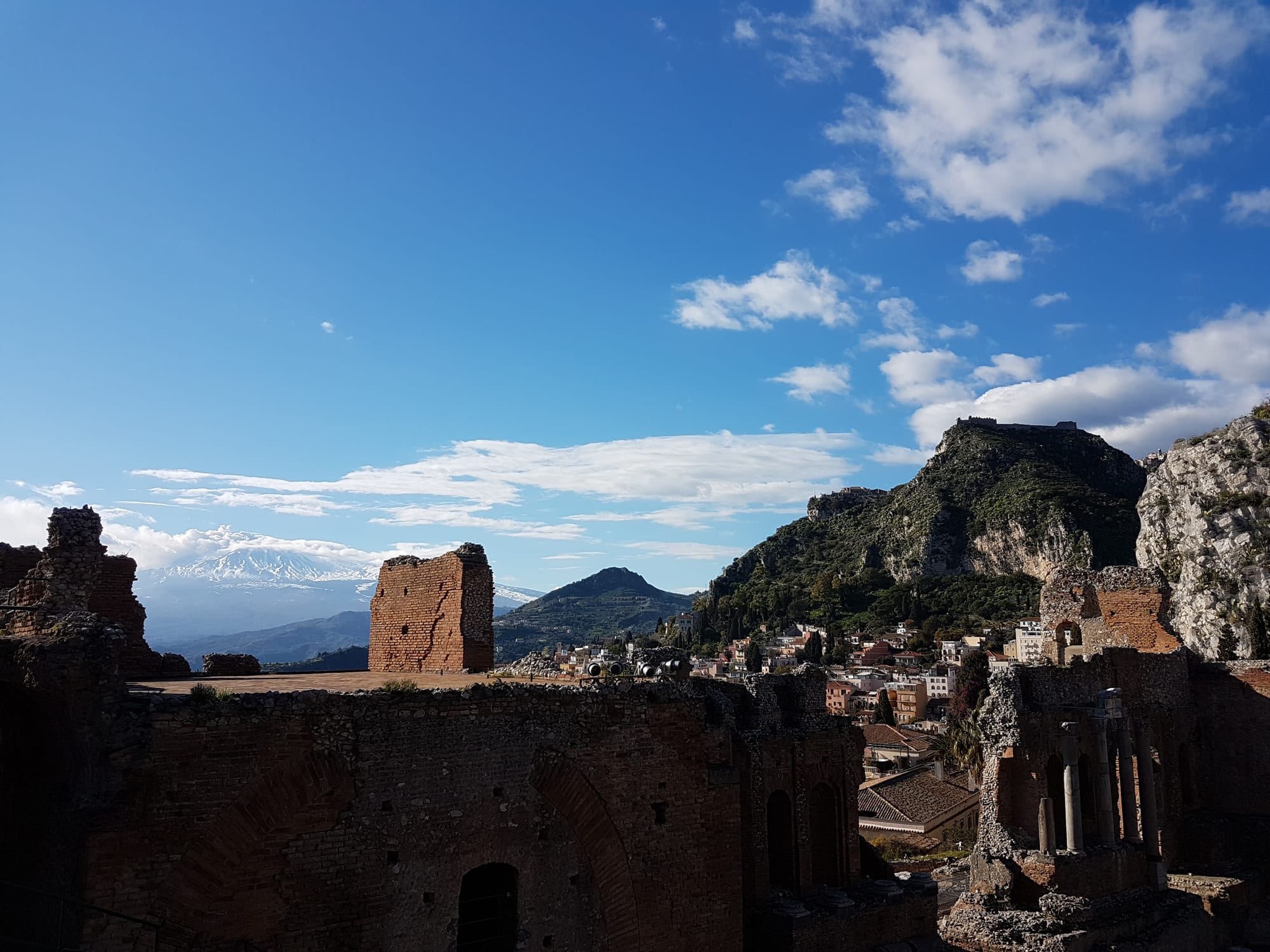 A ruined Greek theatre with a smoking volcano framed between its broken columns