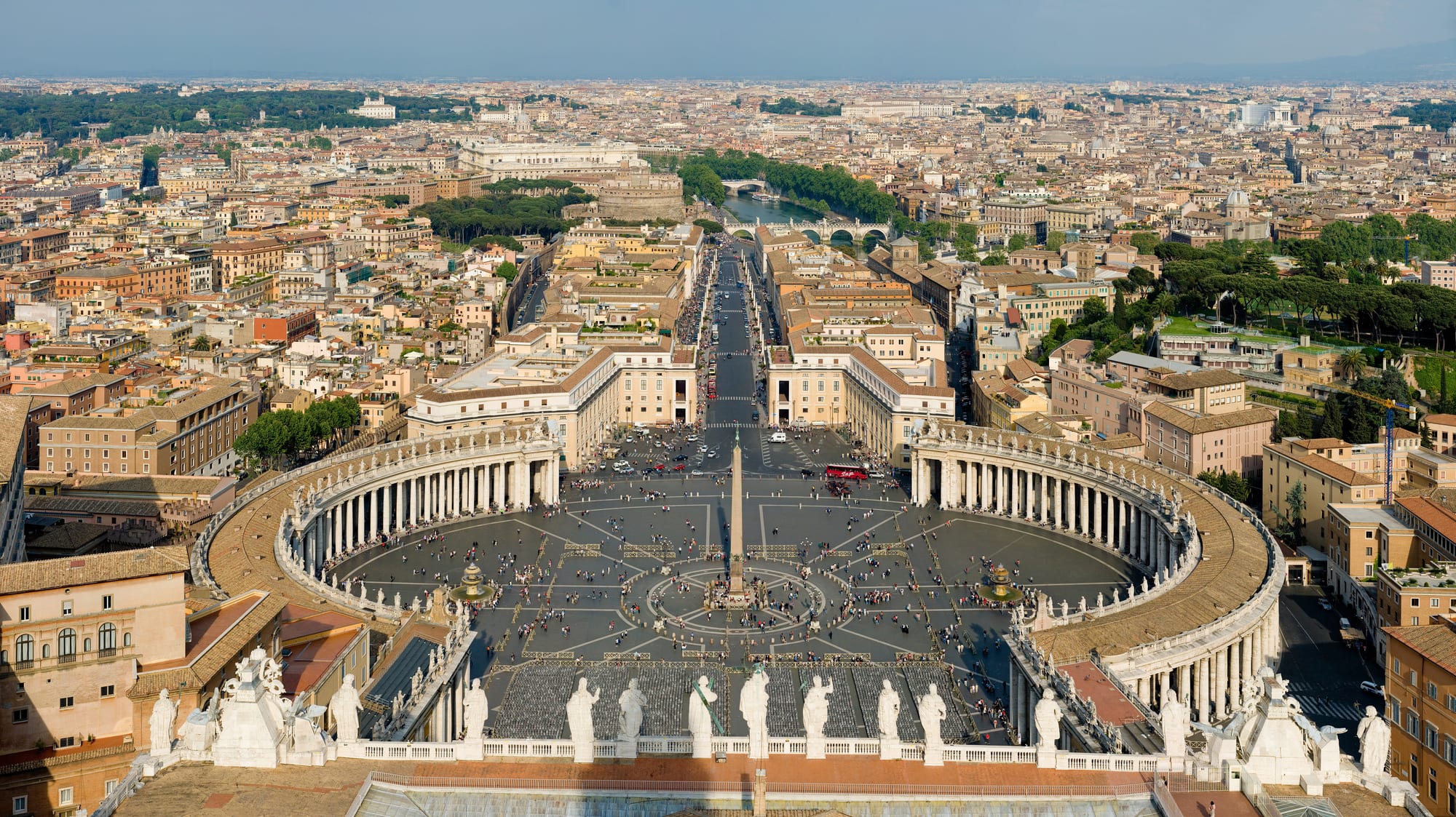An oval colonnaded square with an obelisk and fountains in front of a great domed basilica