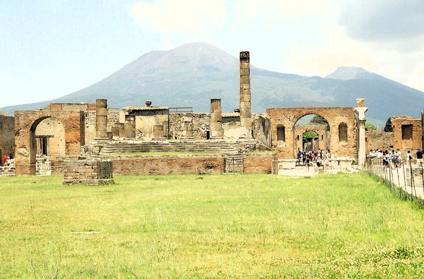 Excavated Roman streets and roofless stone houses with a broad volcano behind