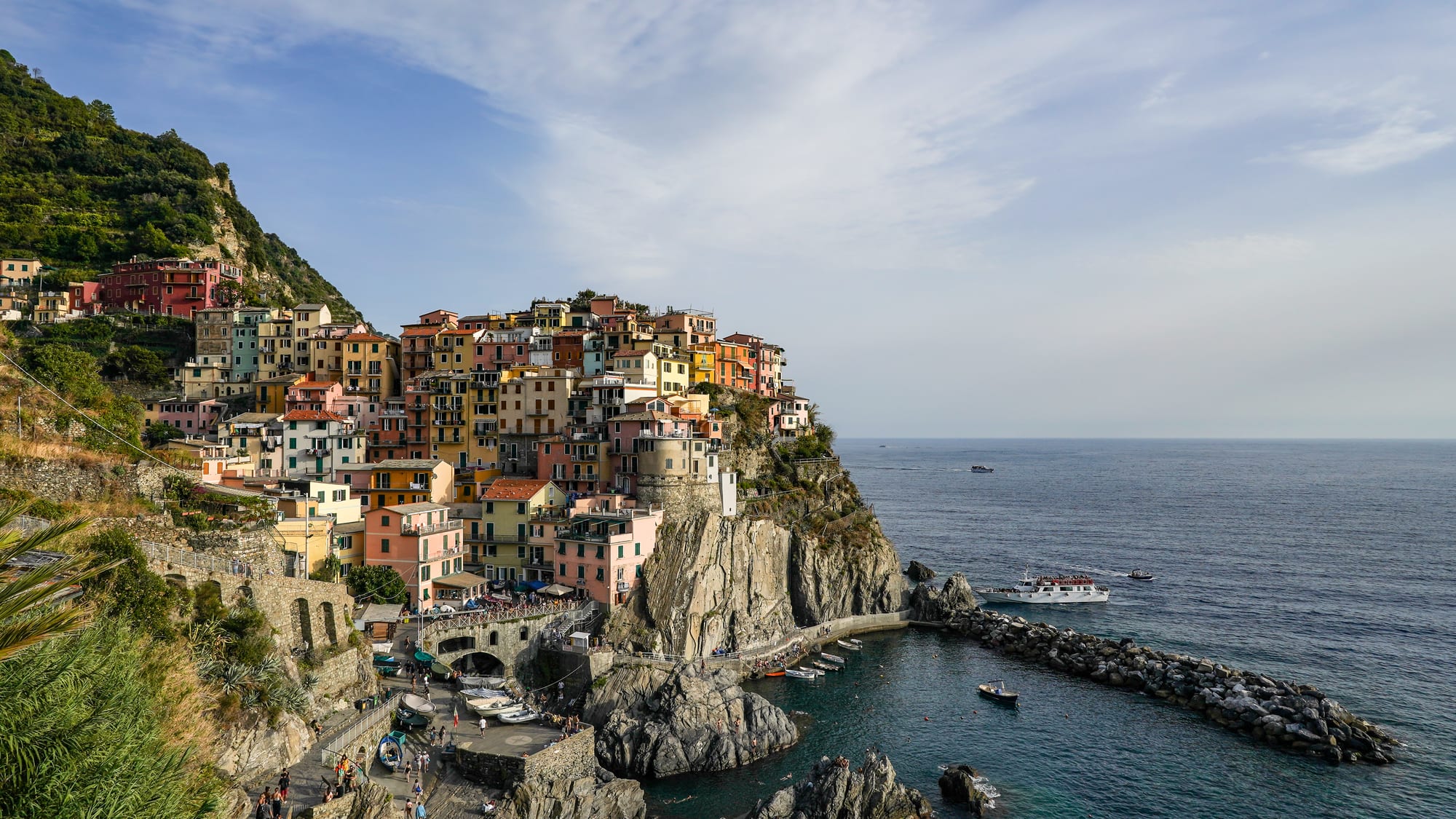 Pastel houses stacked on a cliff above a tiny rocky harbour, terraced vineyards behind