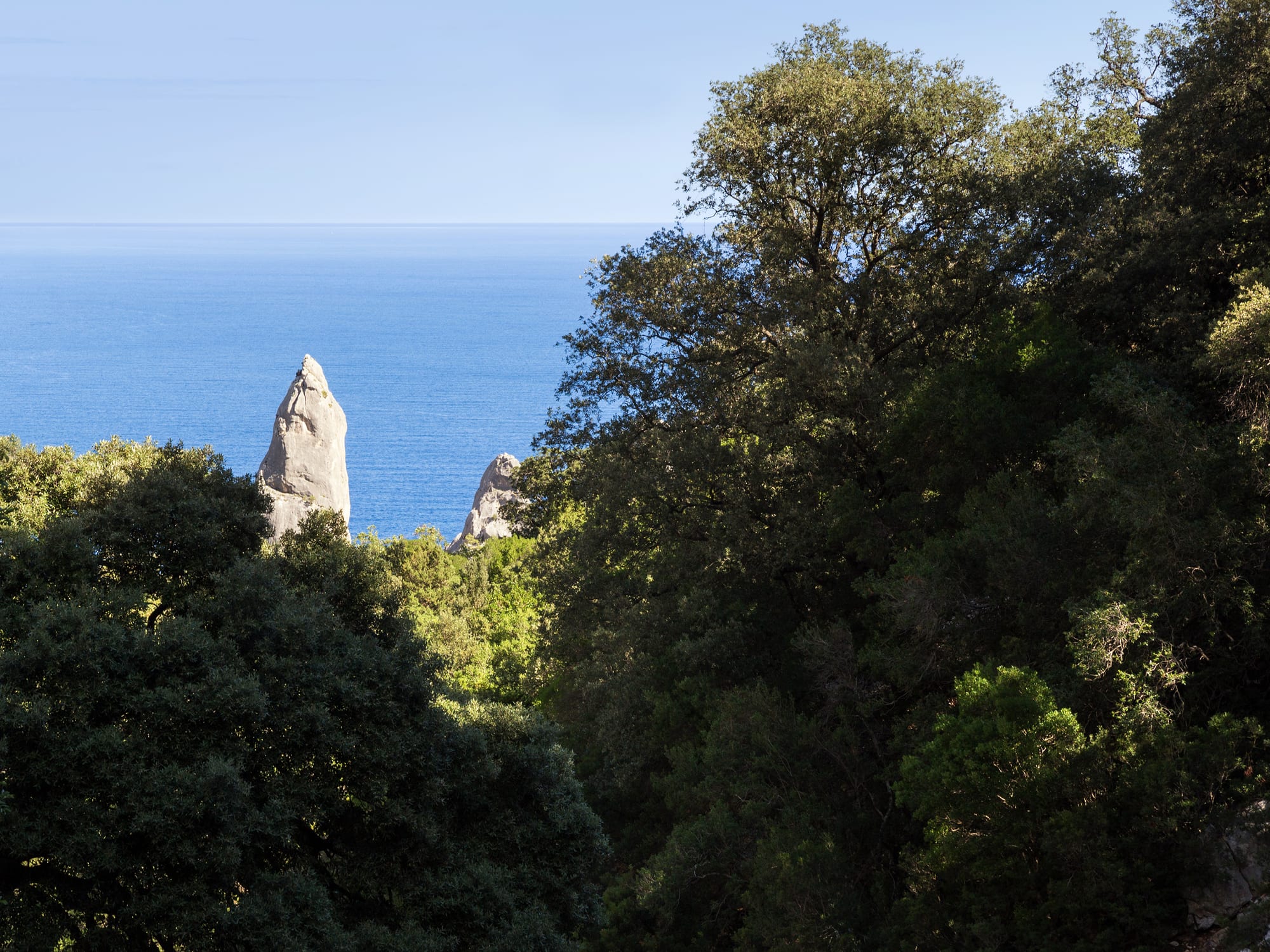 A tiny white pebble cove with a limestone pinnacle rising beside brilliant blue water