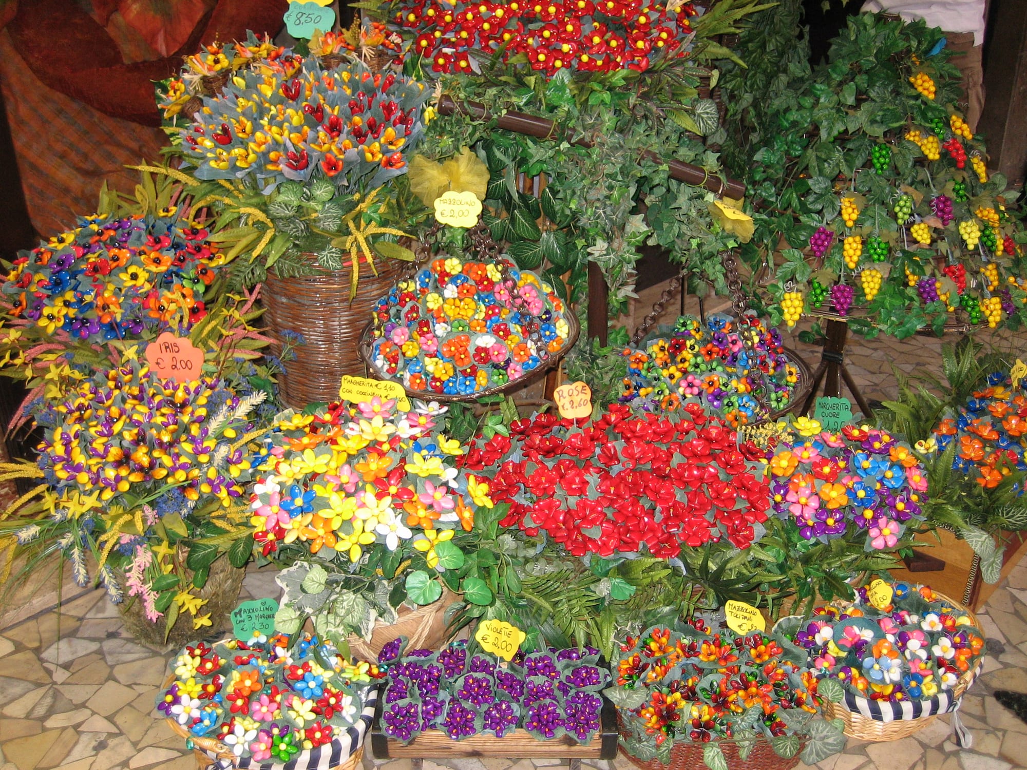 Baskets and stands filled with sugared almonds shaped and coloured to look like bouquets of flowers and bunches of grapes, with small price tags