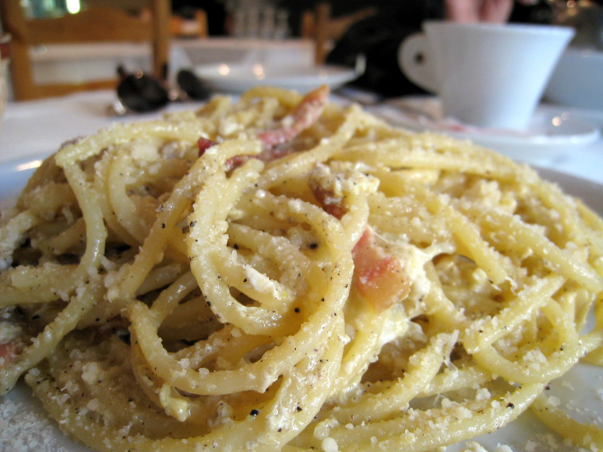 A plate of spaghetti coated in a creamy egg and cheese sauce with flecks of cured pork