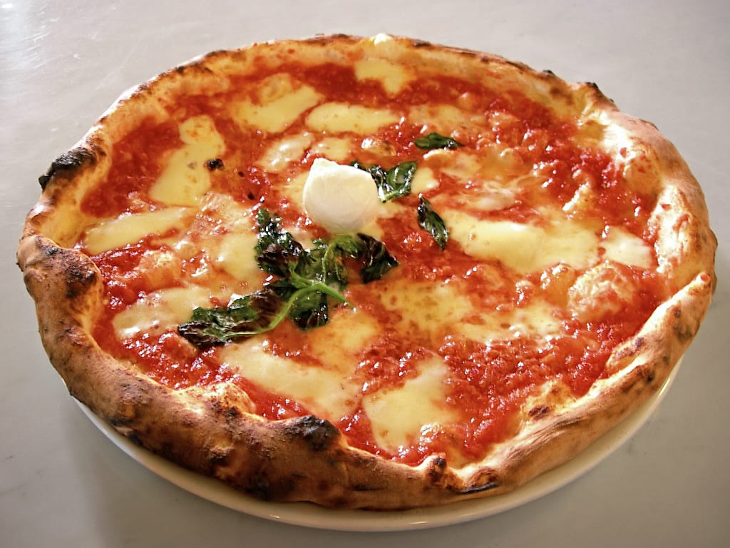 A round pizza topped with tomato sauce, mozzarella and basil leaves