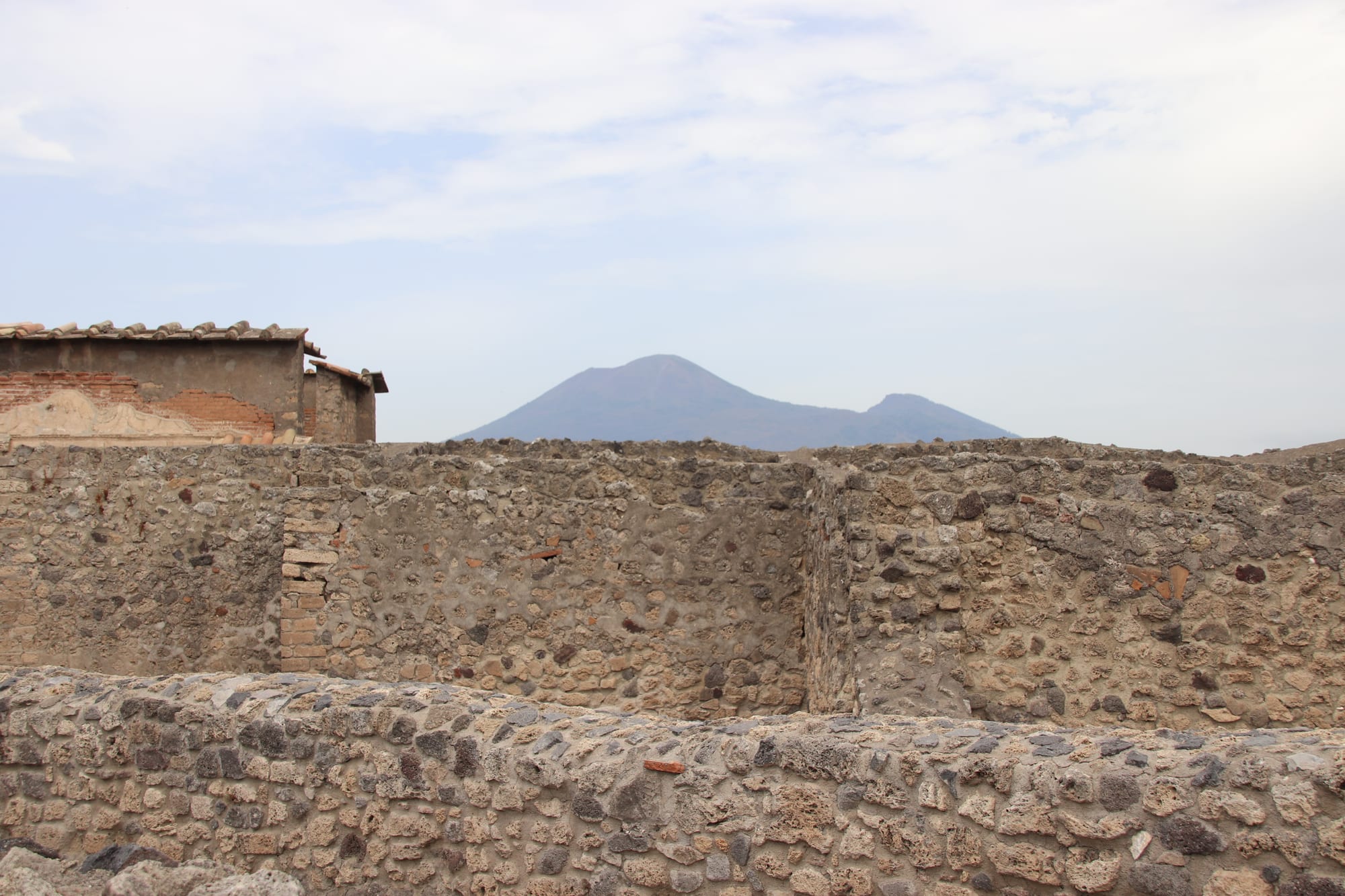 Excavated streets and roofless houses of Pompeii with the cone of Vesuvius behind