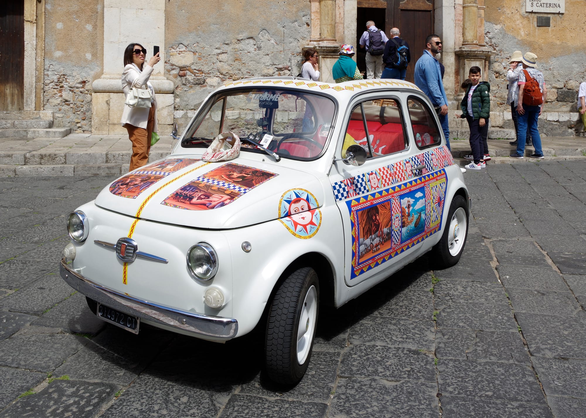 A tiny pale-blue 1950s Fiat 500 car parked on a street
