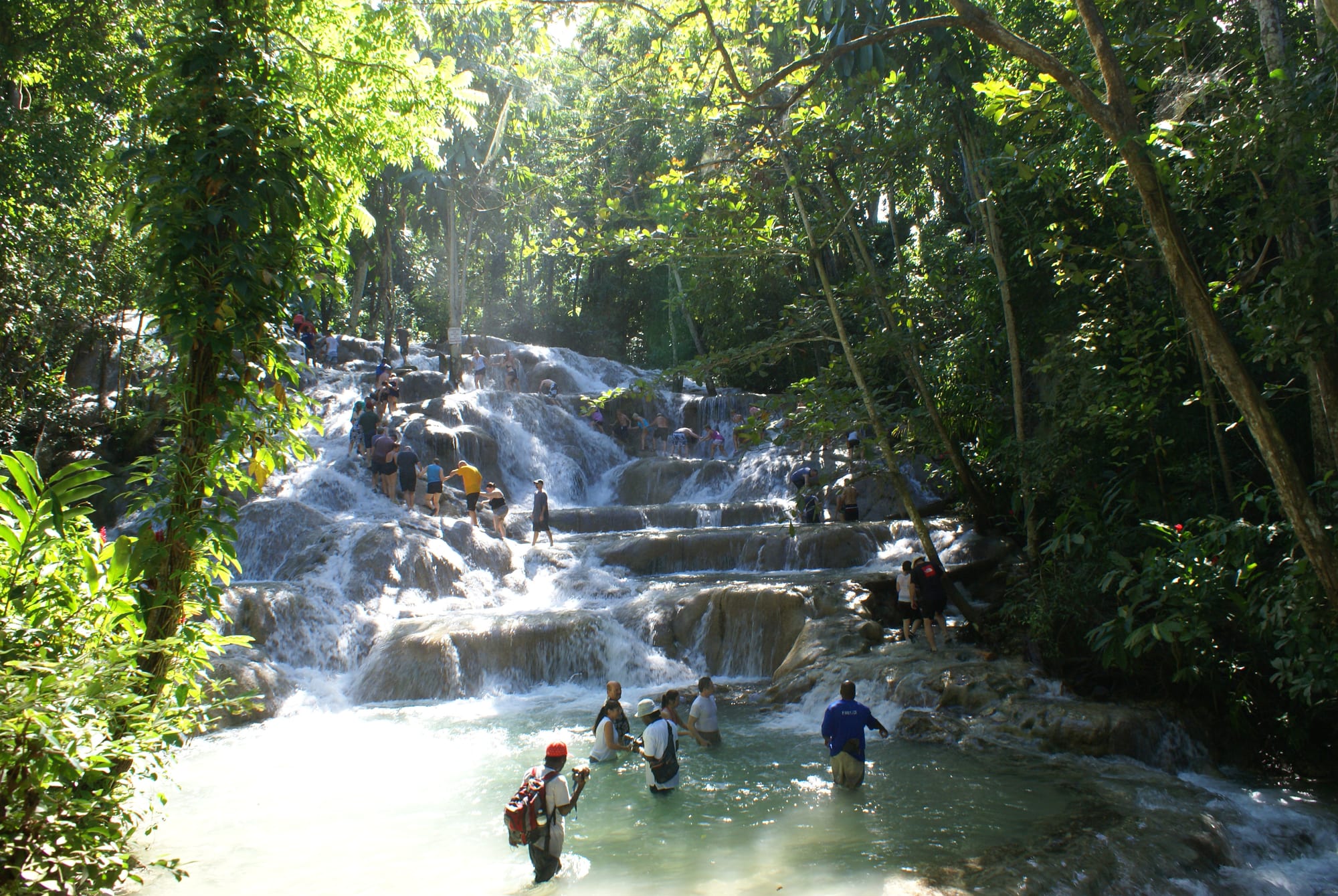 A line of people holding hands, climbing up a rushing waterfall over rock ledges