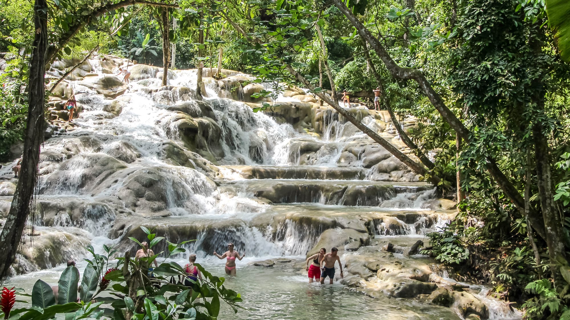 A wide terraced waterfall spilling down rock steps into pools, surrounded by green forest