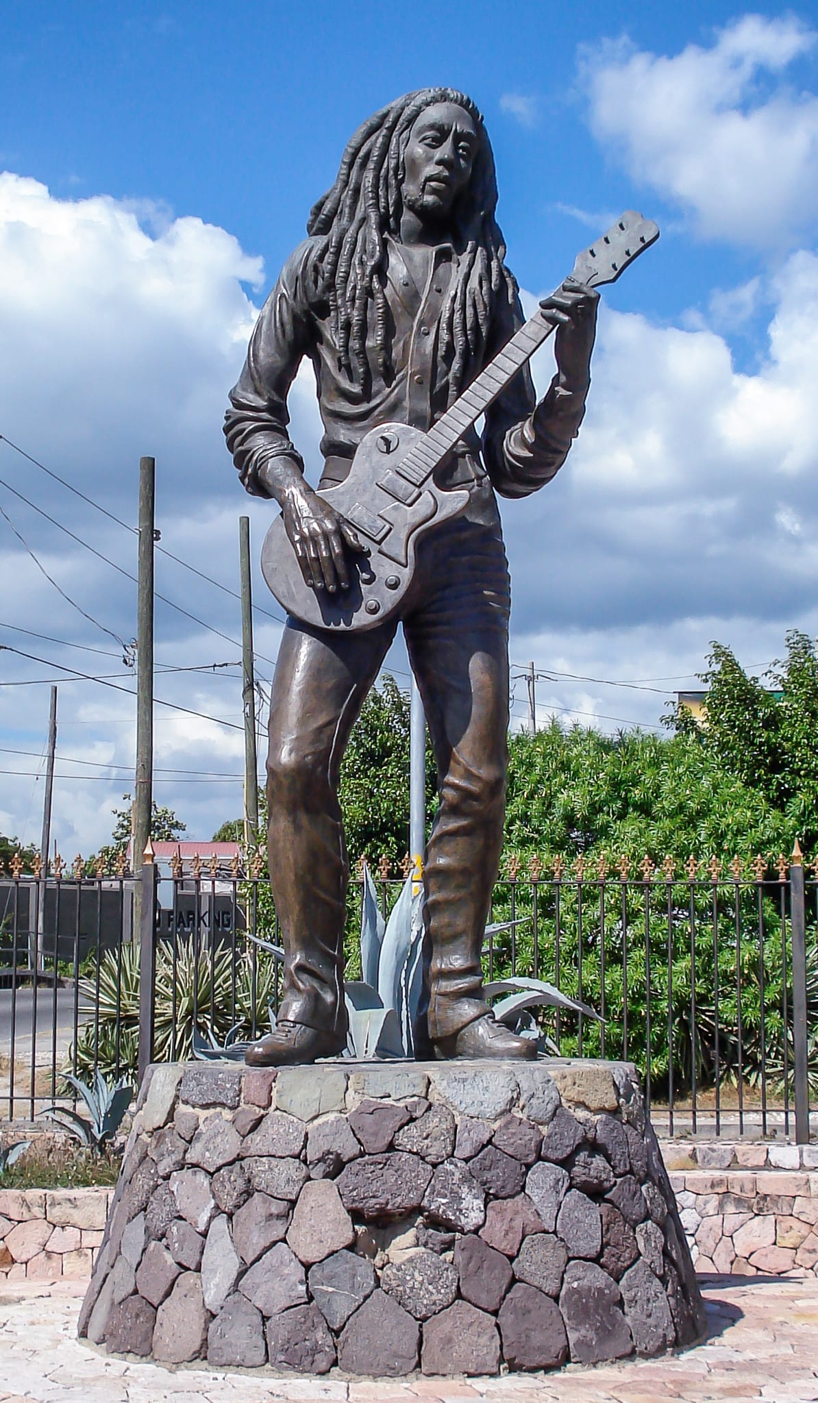 A bronze statue of Bob Marley with a guitar, on a plinth in a green park