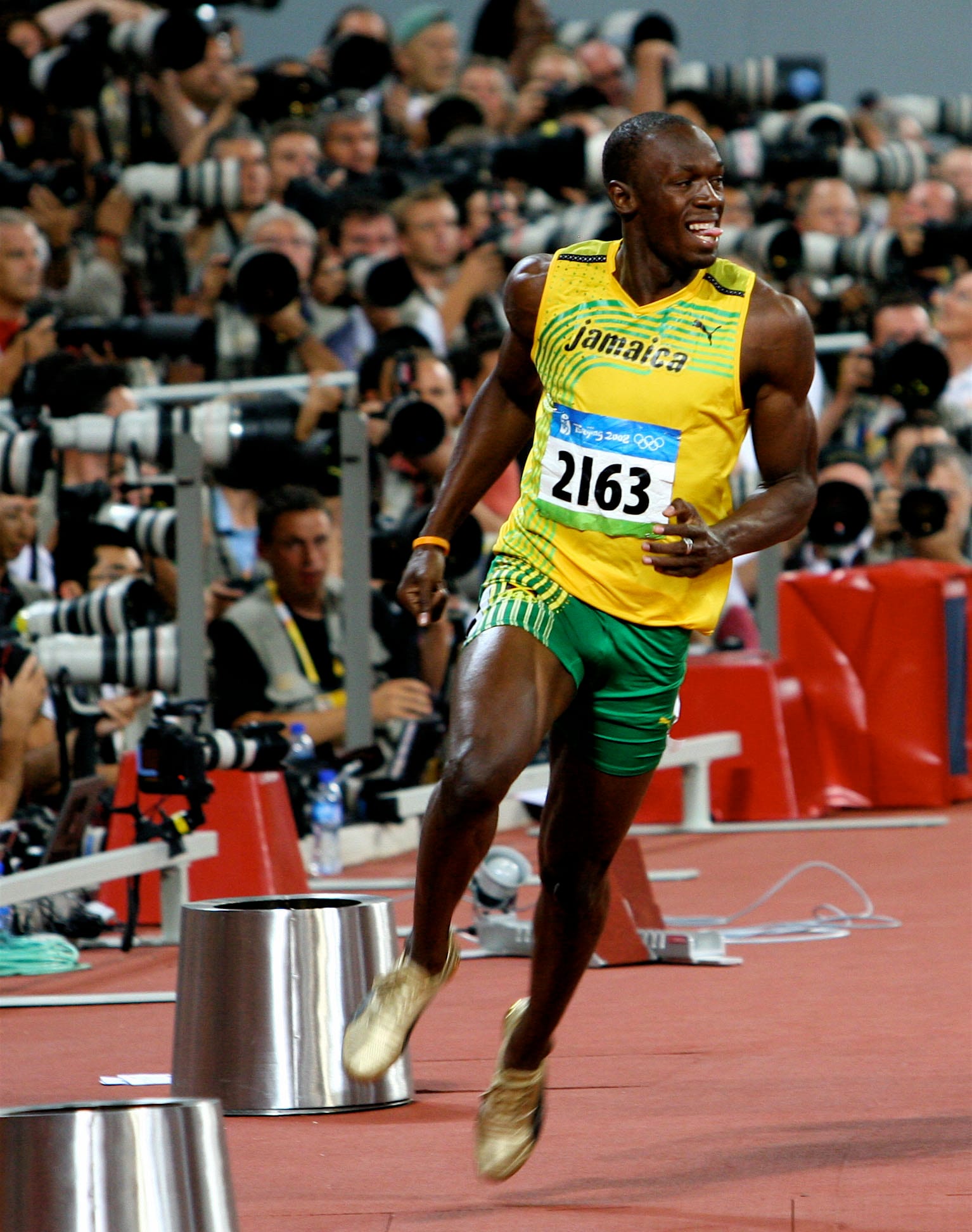 Usain Bolt in a yellow Jamaica singlet and gold spikes running past a bank of photographers at the Olympics