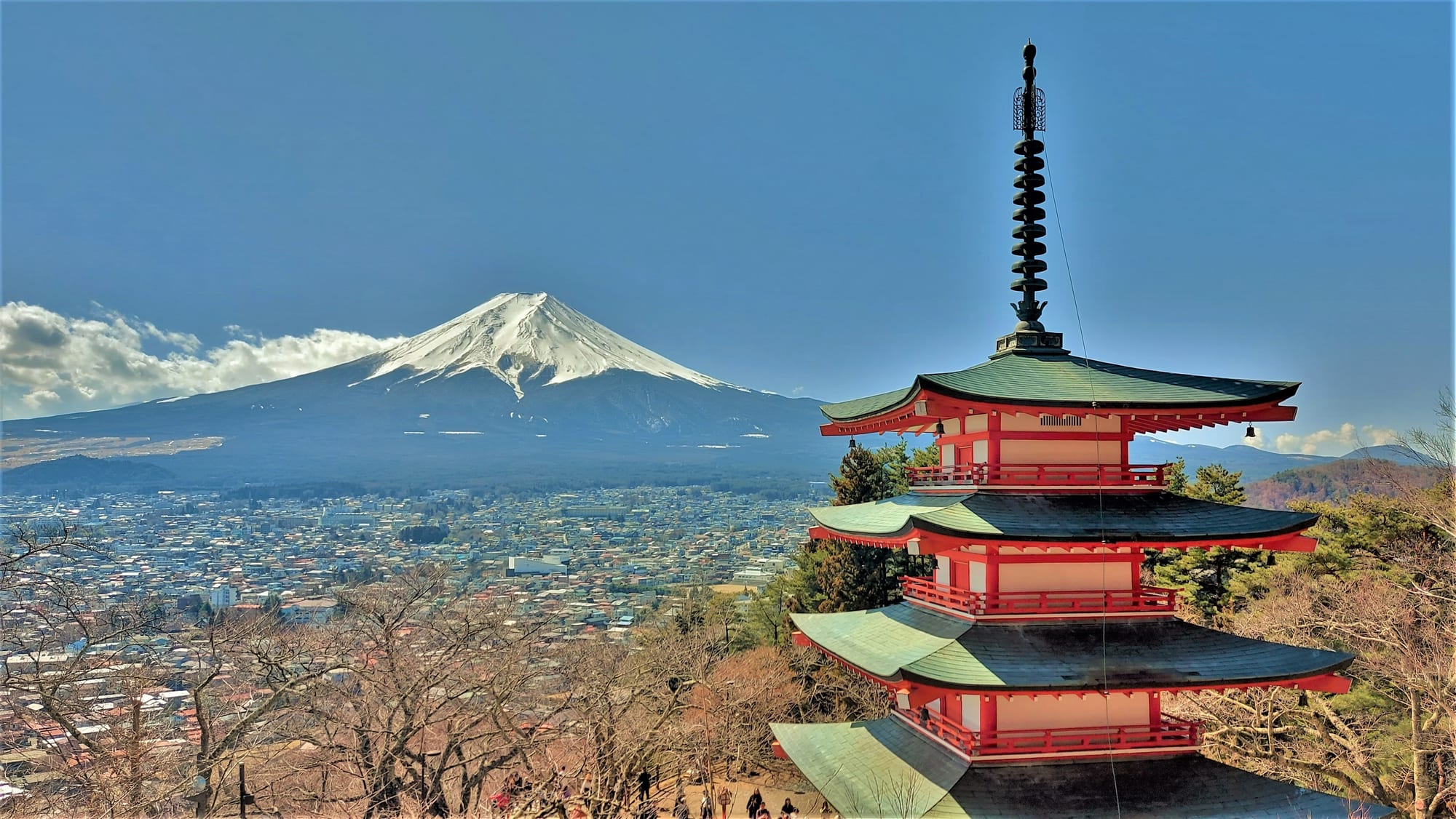 A five-storey red pagoda on a hillside with a snow-capped symmetrical volcano behind