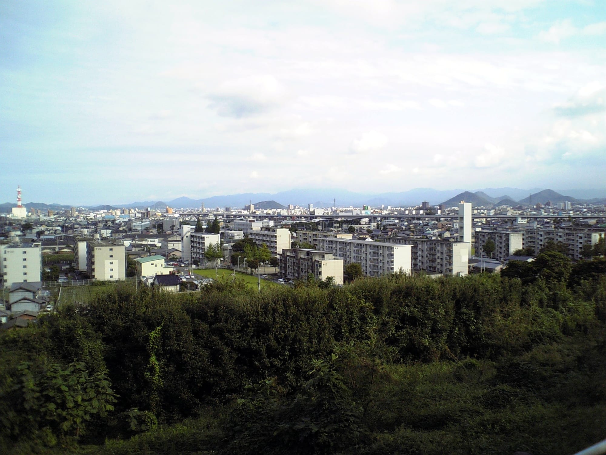 A view over a Japanese apartment housing complex (danchi) with multiple mid-rise blocks, seen from a hillside above the city