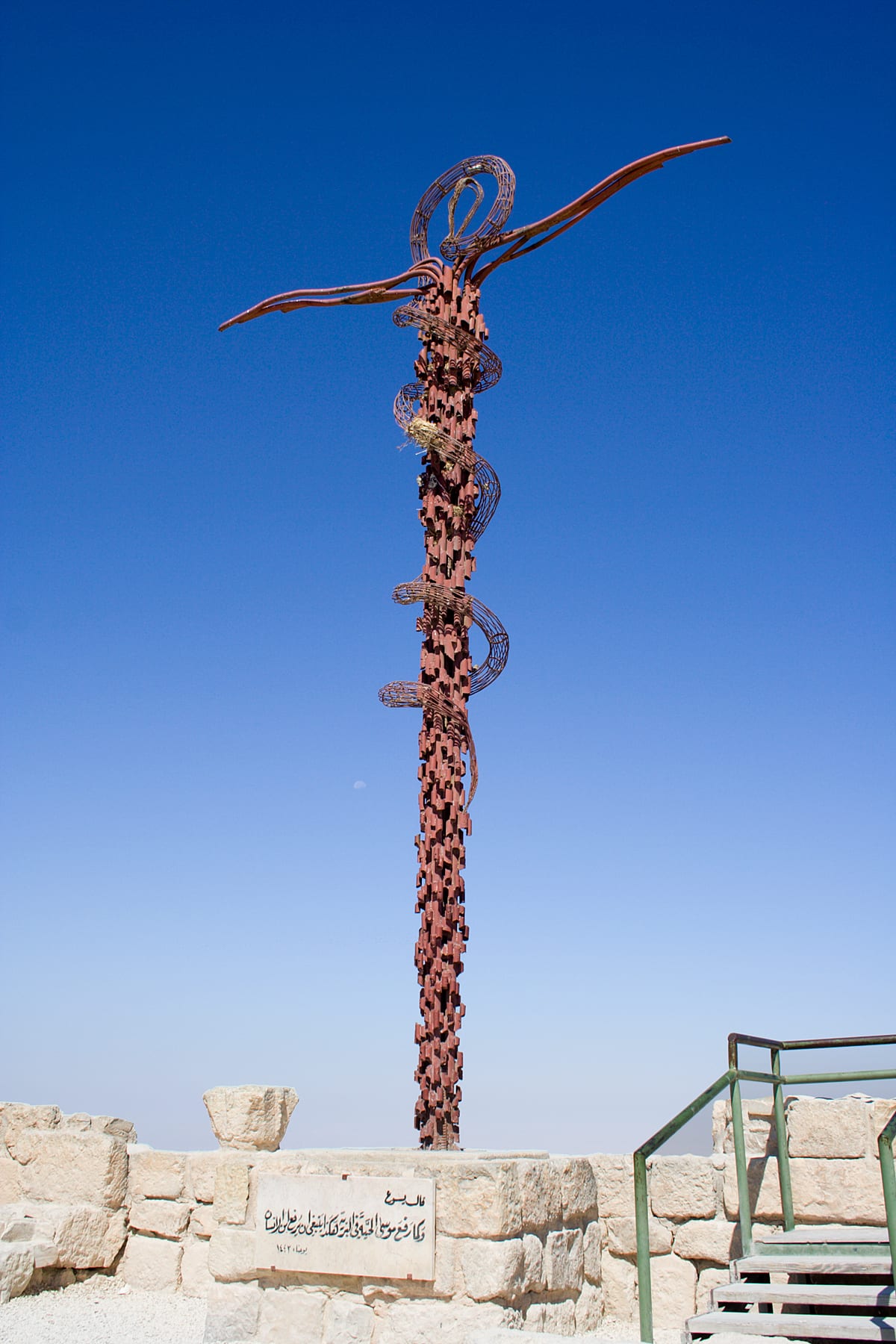 A hilltop memorial sculpture of a serpent-entwined cross against a clear sky