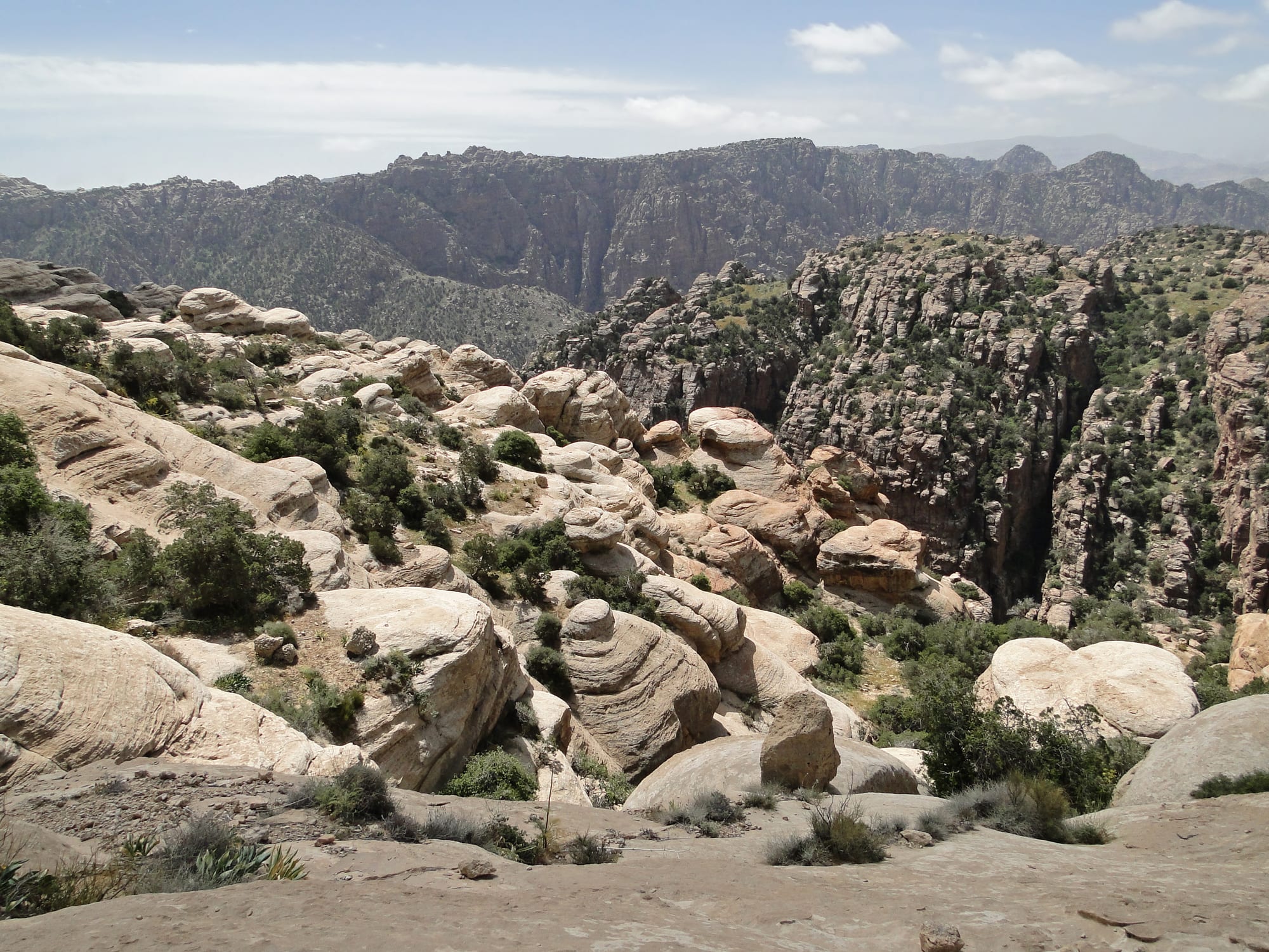 A deep desert valley of red and pale rock layers descending toward a hazy horizon