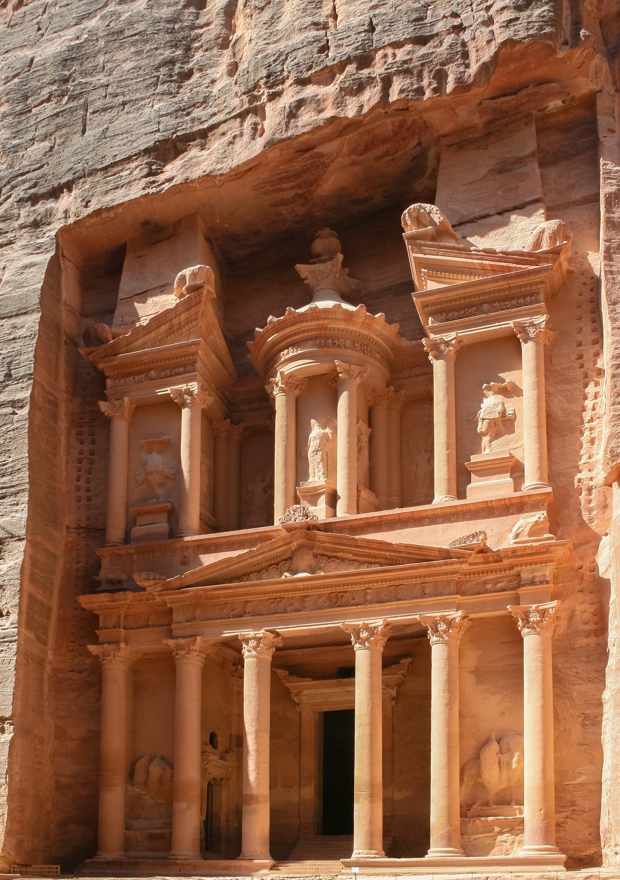 An ornate classical facade carved directly into a towering rose-coloured sandstone cliff