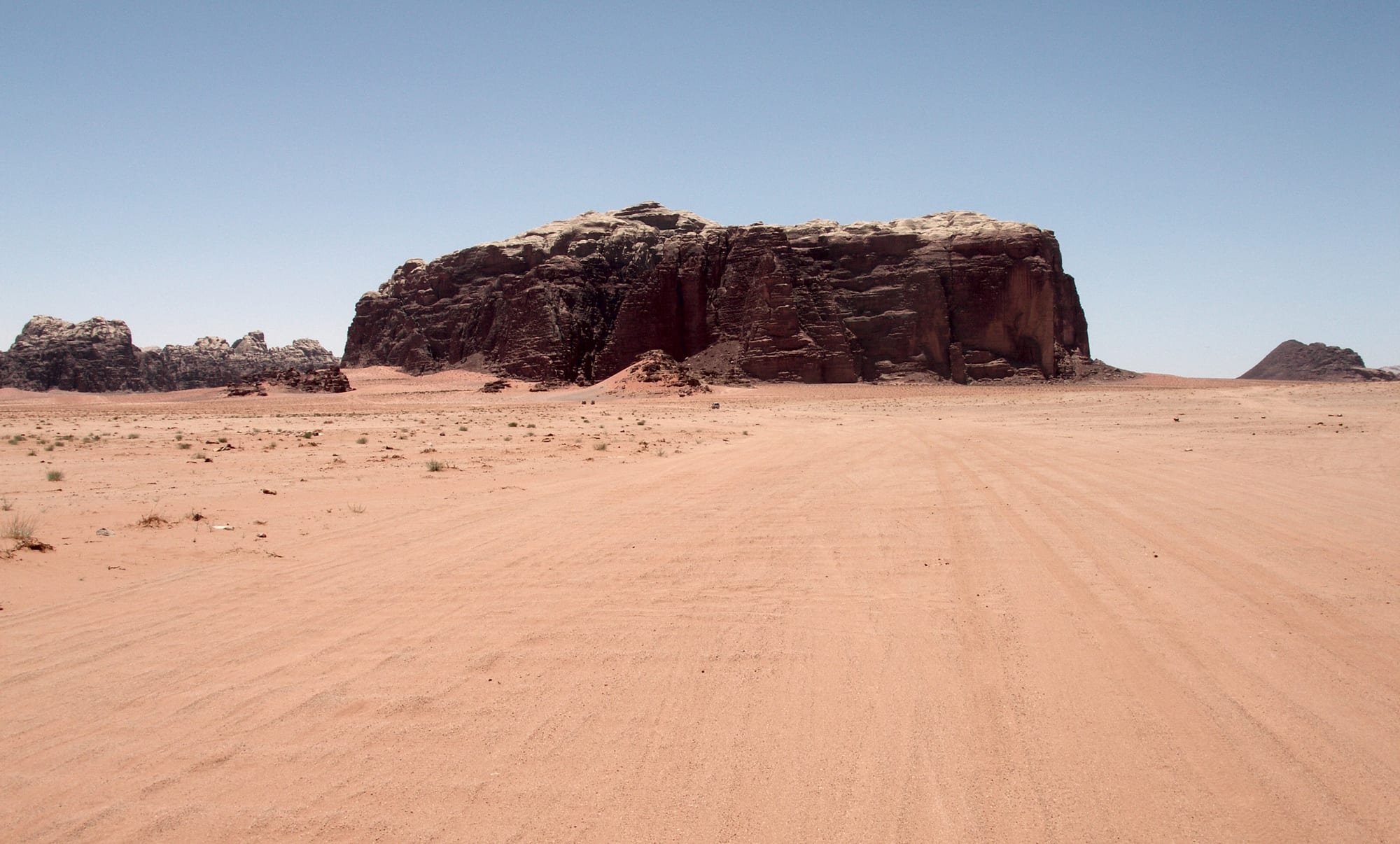 Vast red sand plains between towering, weathered sandstone and granite mountains