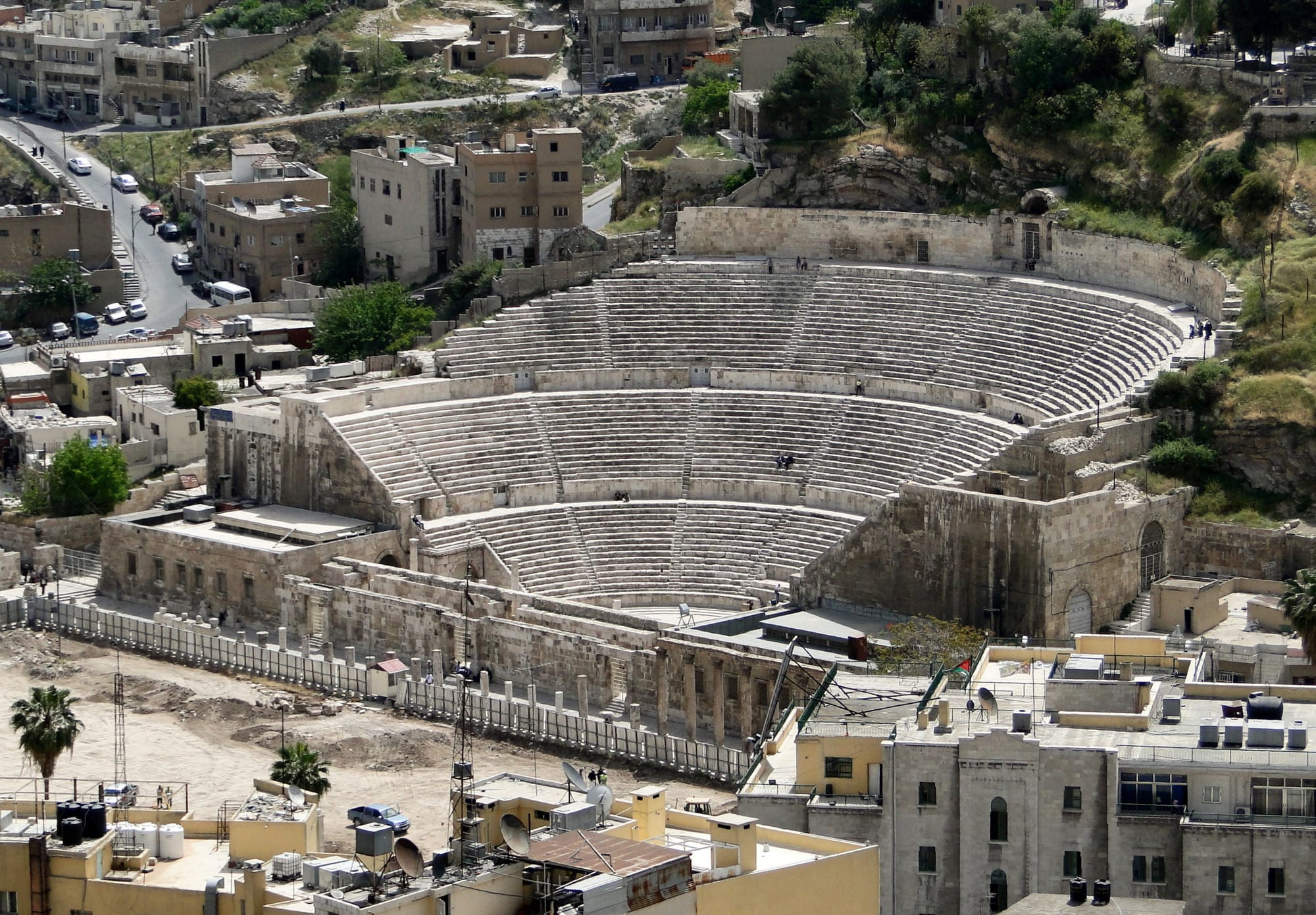 A large Roman theatre of steep stone seating cut into a hillside in a modern city