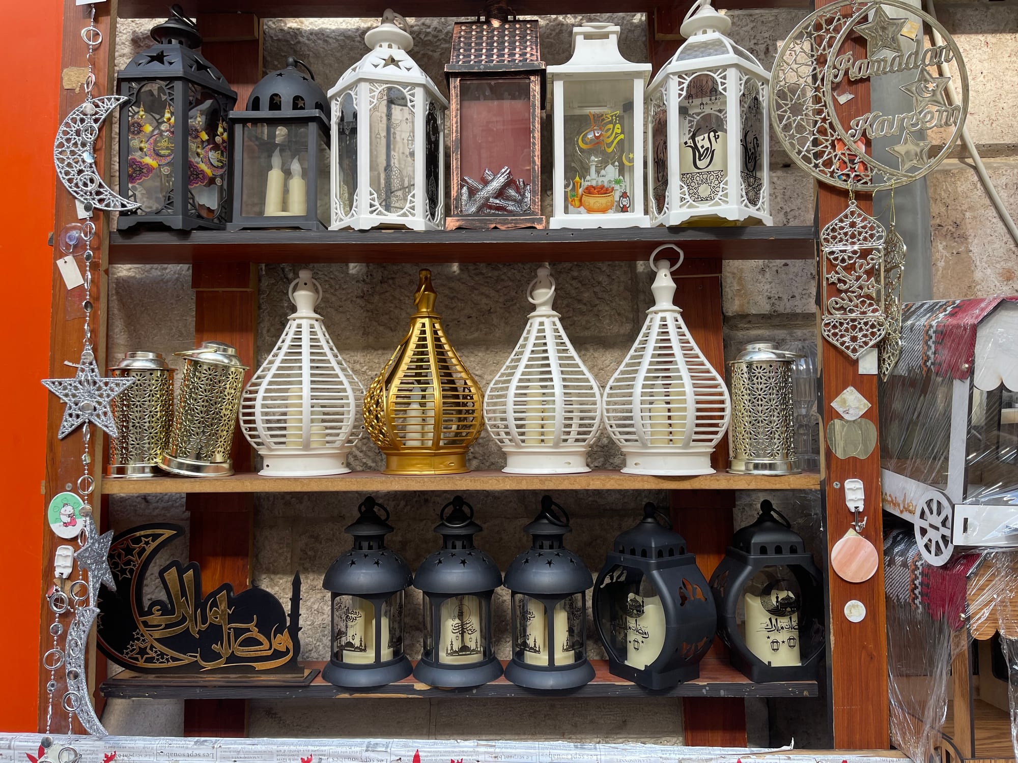 Shelves in a shop filled with decorative lanterns in black, white, gold and silver, with crescent-moon ornaments and a sign reading Ramadan Kareem