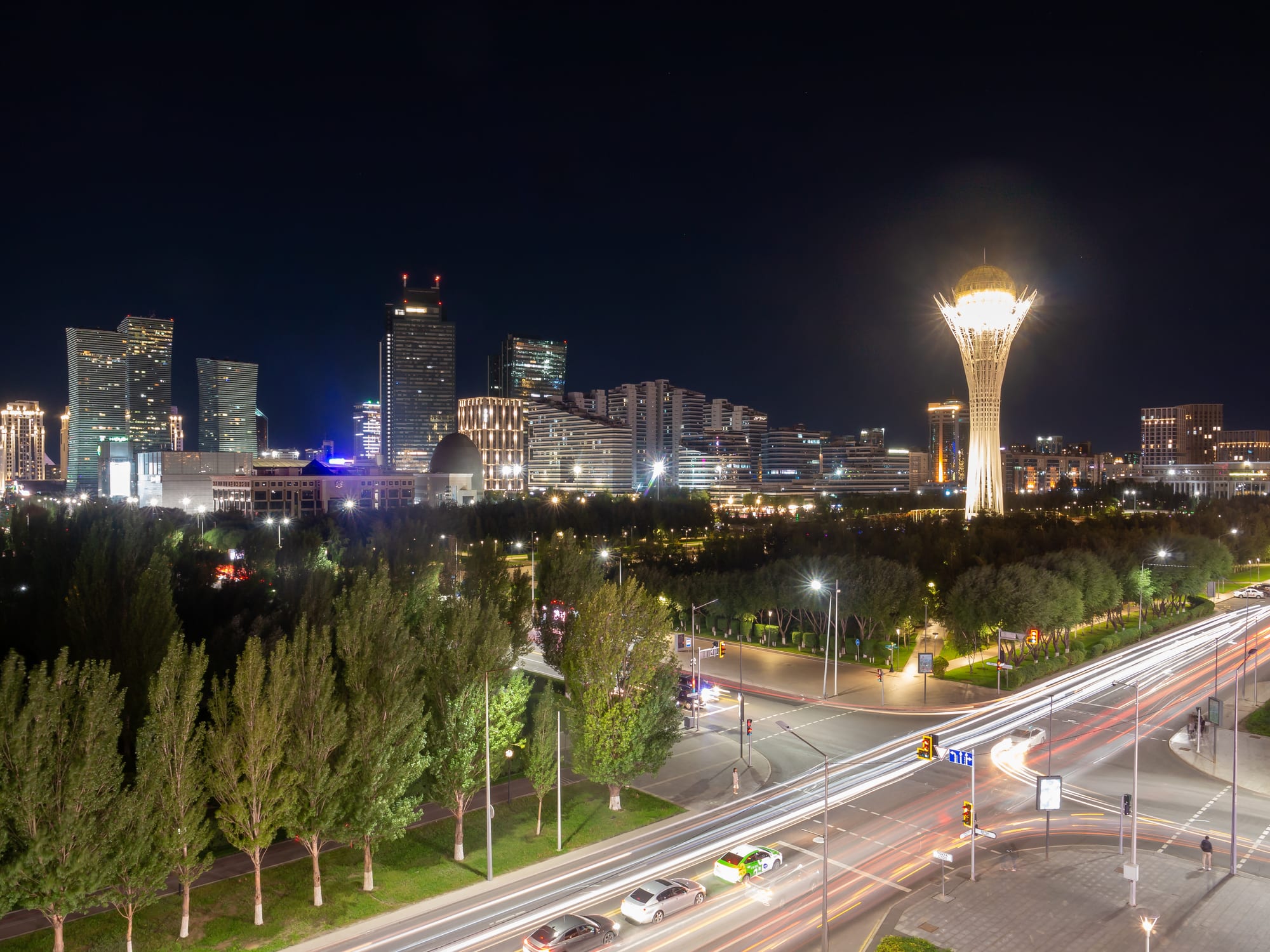 A lit-up city skyline at night with the golden Bayterek Tower rising above it