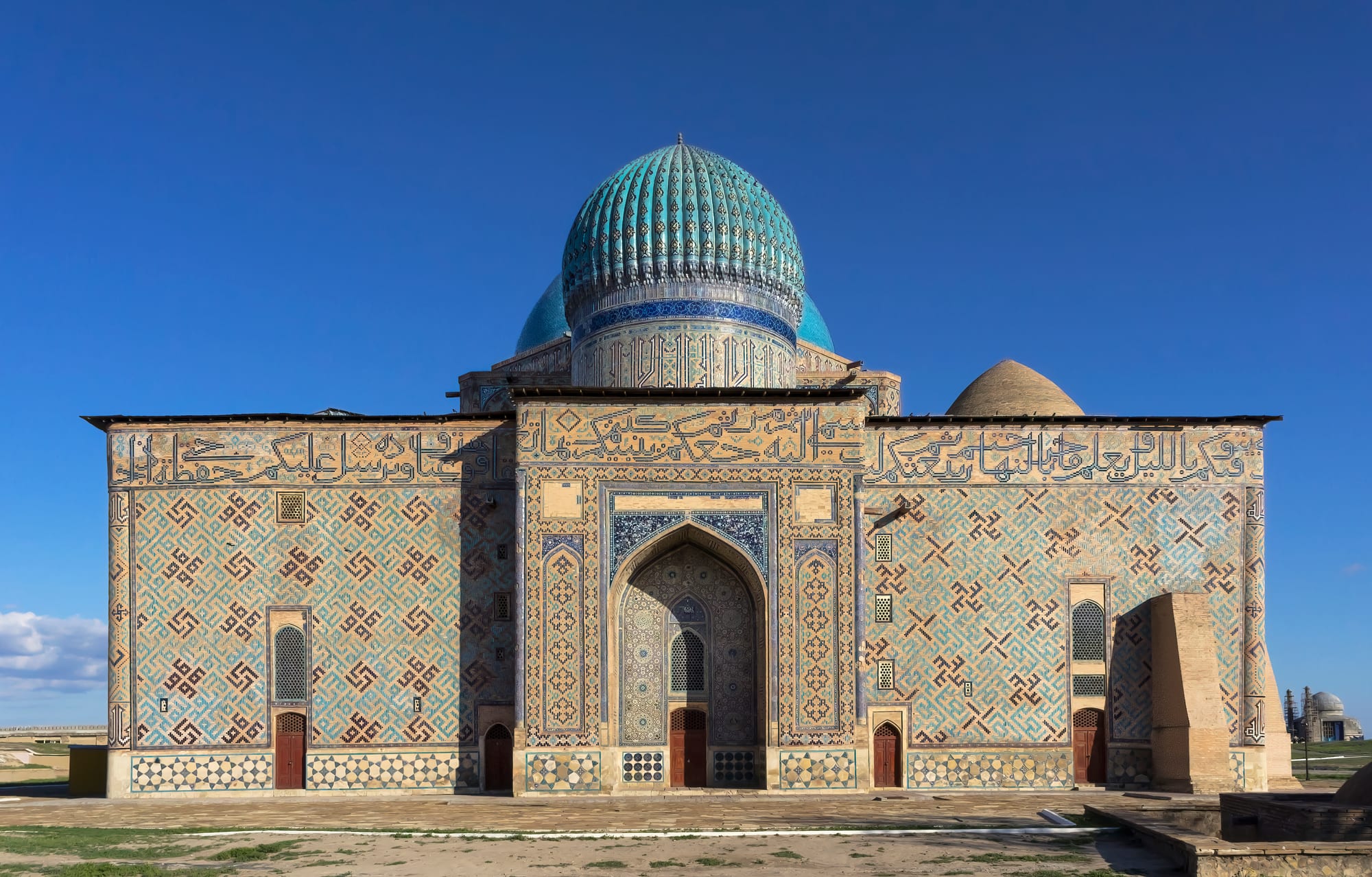 A massive turquoise-domed brick mausoleum with a huge unfinished portal arch