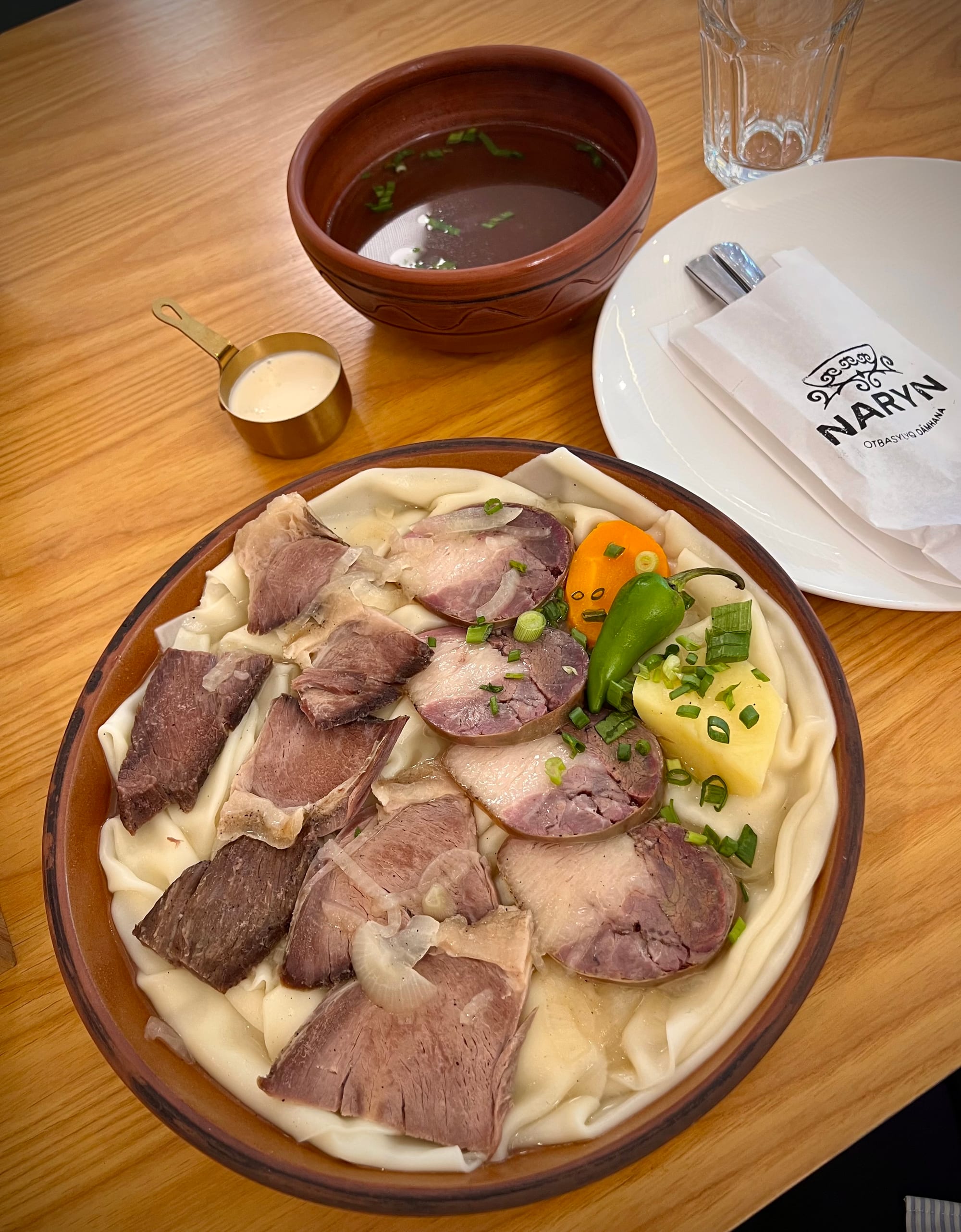Boiled meat and wide flat noodles topped with onions on a large platter