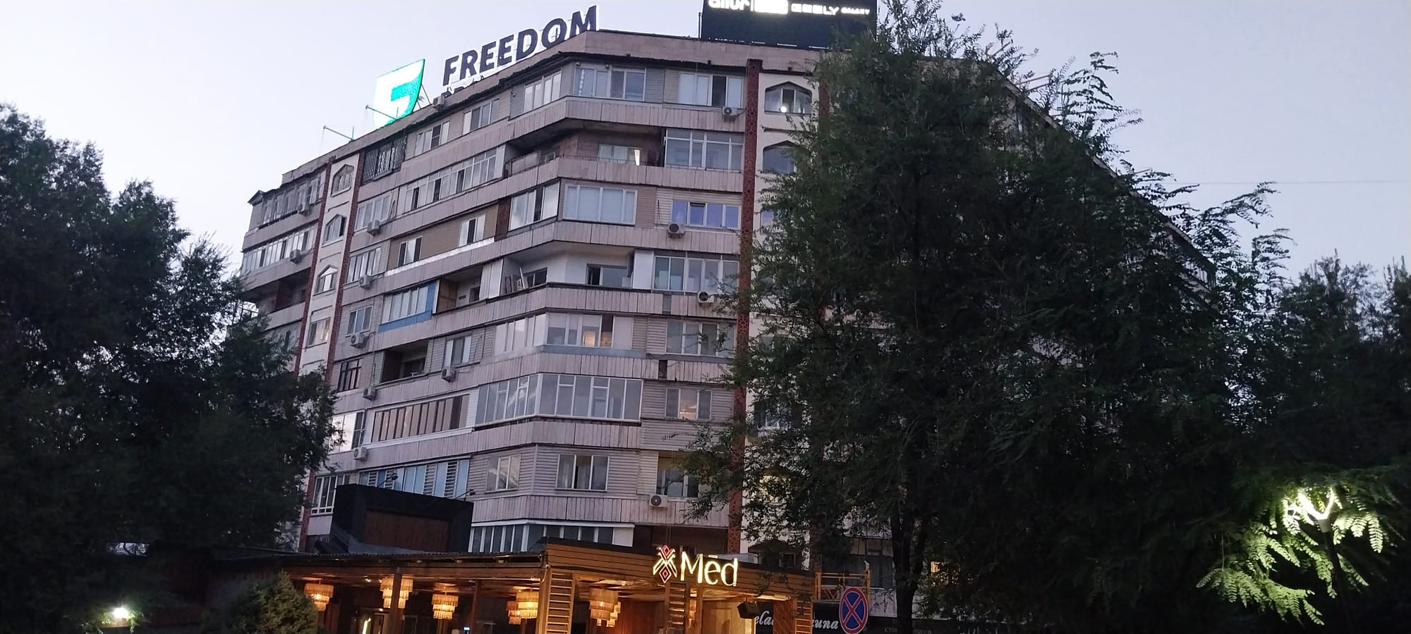 A multi-storey Soviet-era apartment building with rows of balconies, photographed at dusk with trees in front