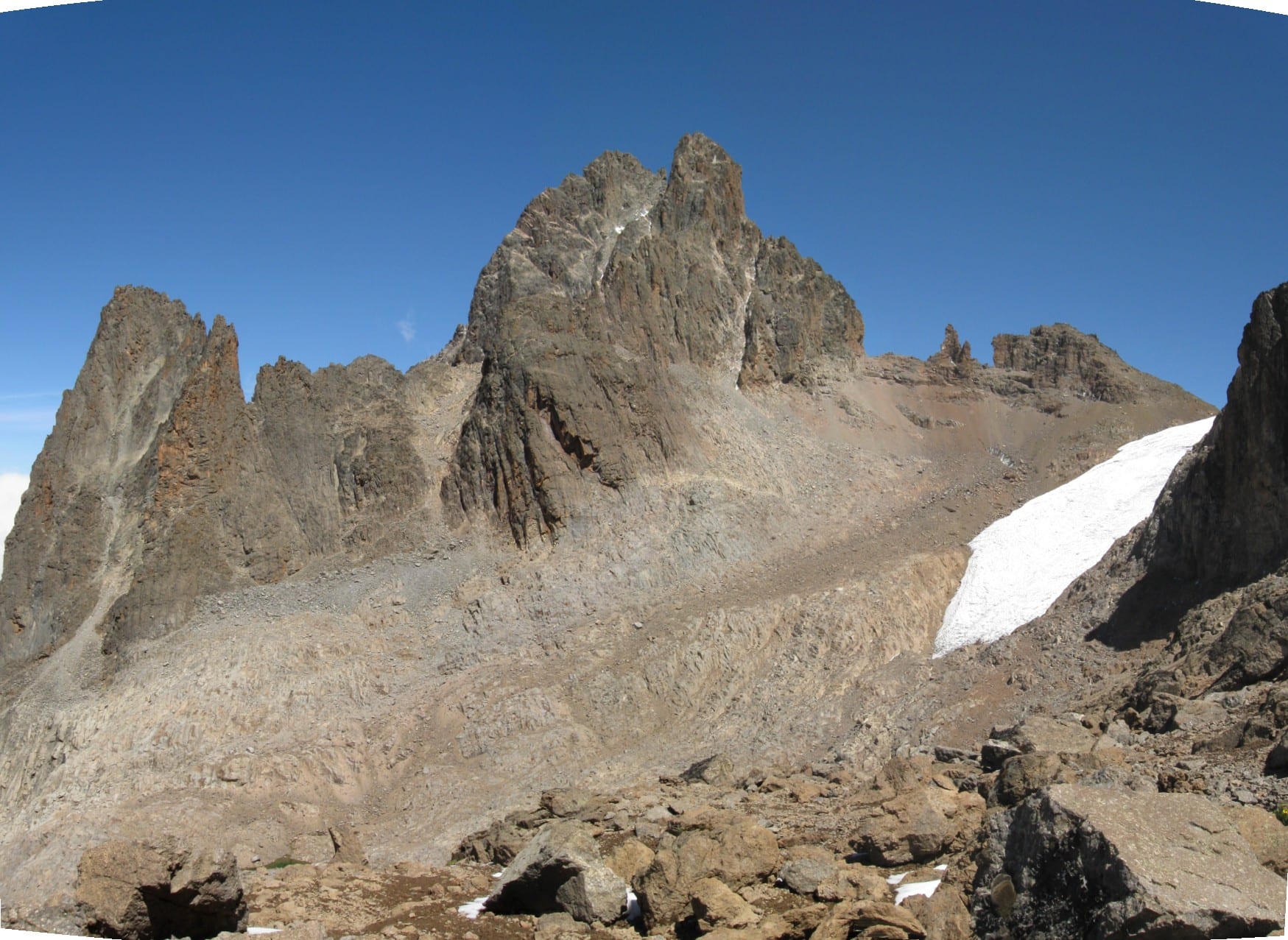 A jagged rocky peak with small glaciers, rising above moorland and forest
