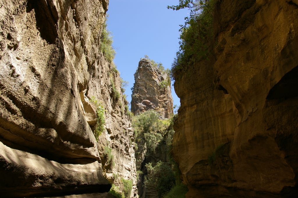 A dry, narrow rock gorge with reddish walls and a sandy floor