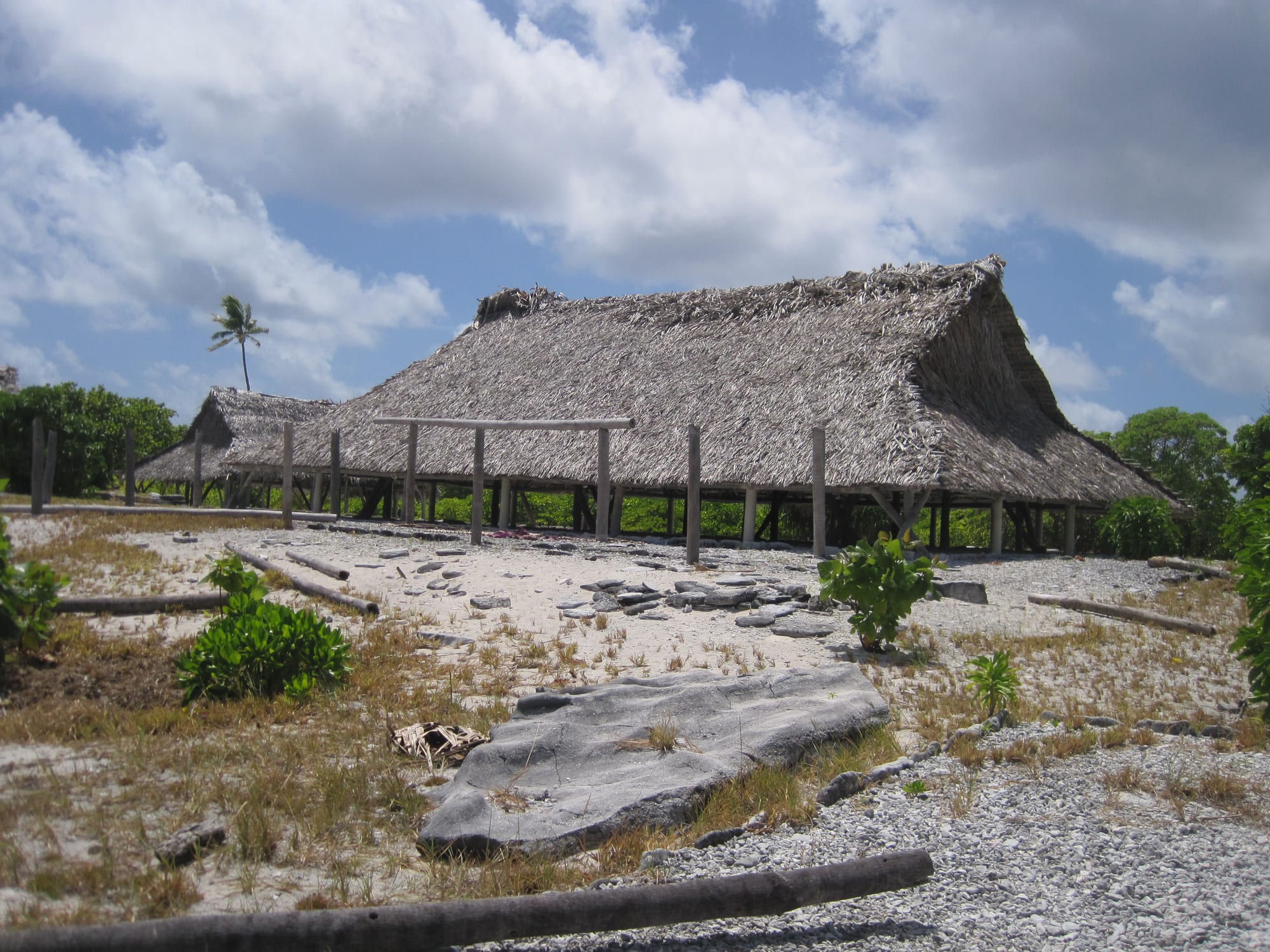 A very large open-sided thatched meeting house with a steep pitched roof on a coral island