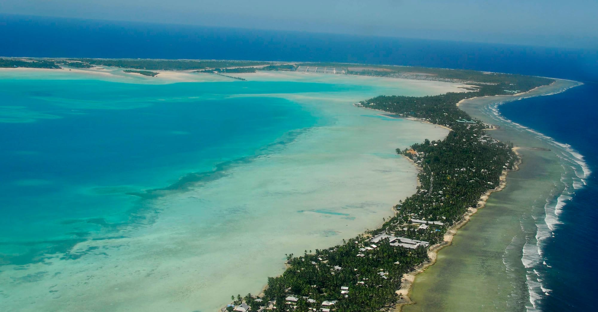 A thin ribbon of densely built land curving through a huge blue lagoon and ocean
