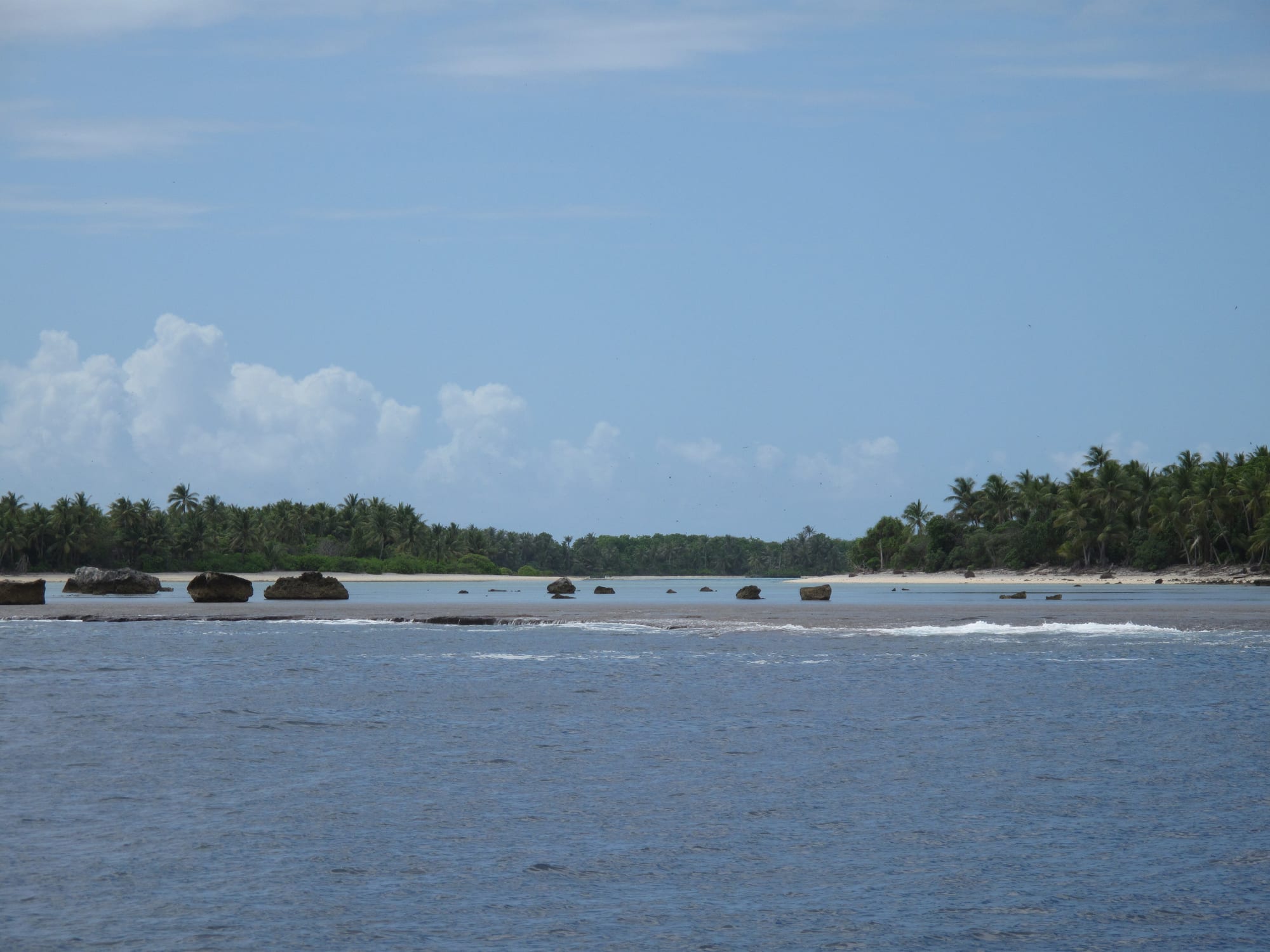 An uninhabited coral island and reef ringed by deep blue open ocean