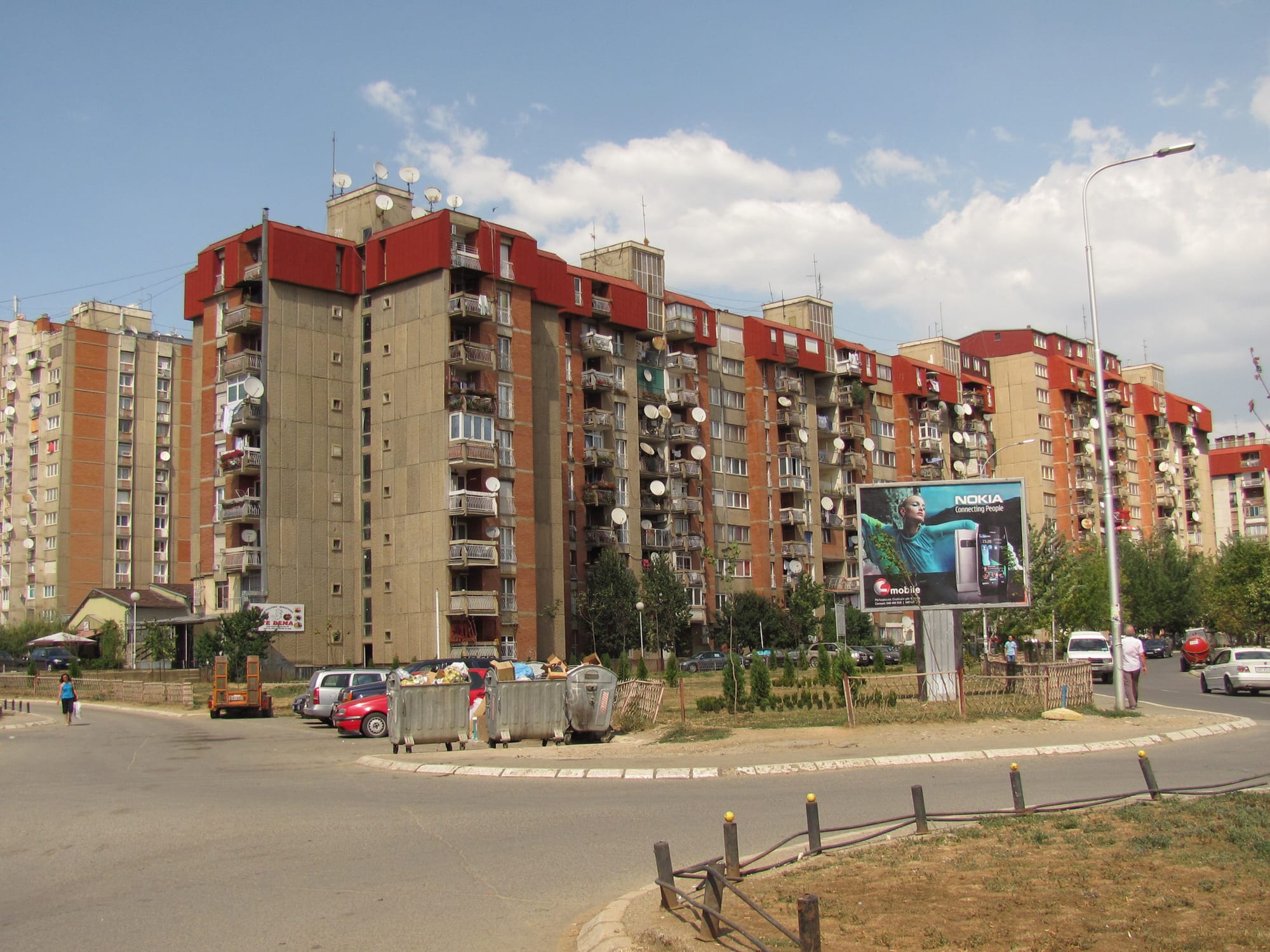 Rows of tall concrete apartment blocks with satellite dishes on every balcony, cars parked below