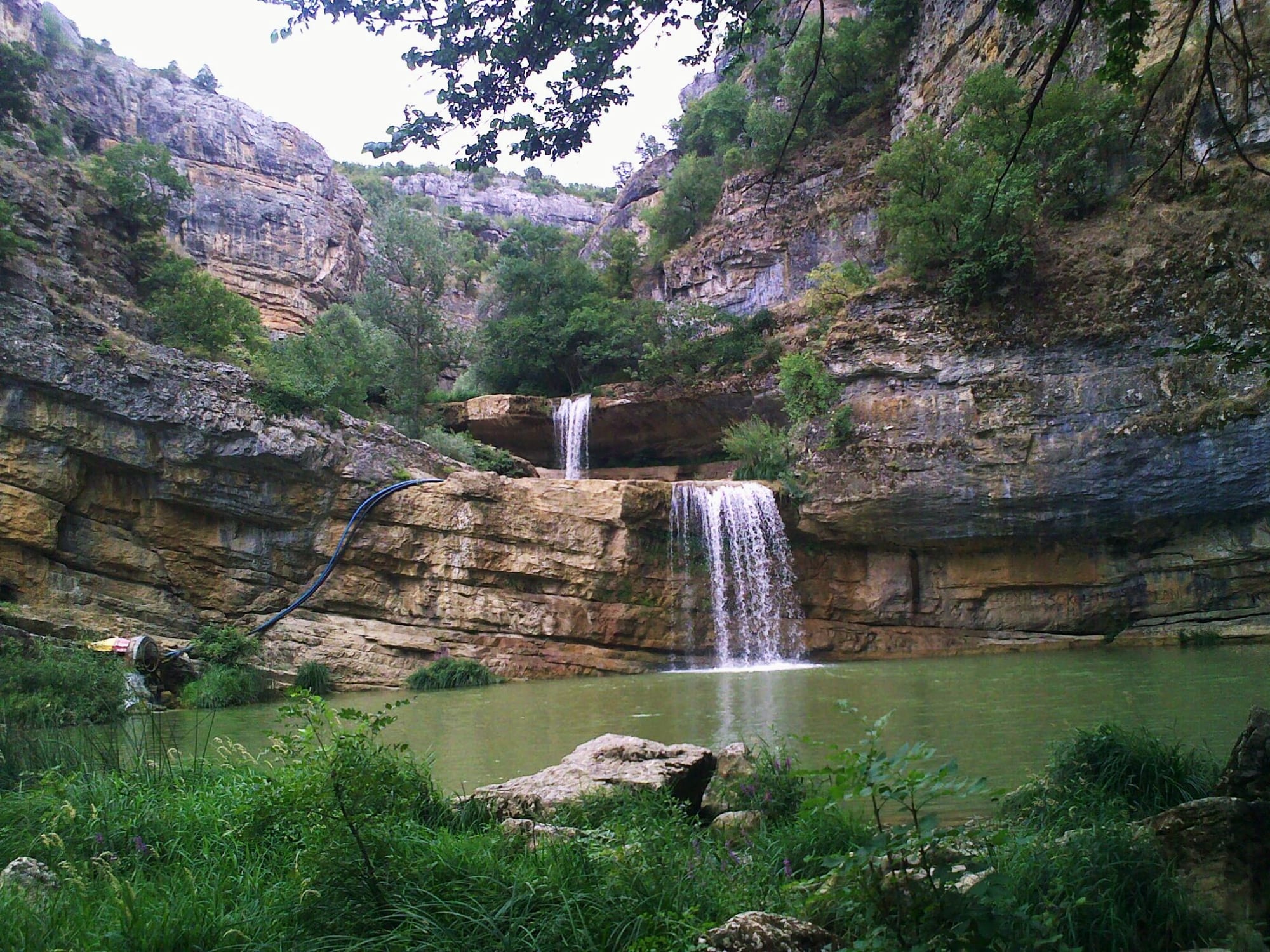 A river dropping through a series of small waterfalls into green pools in a rocky gorge