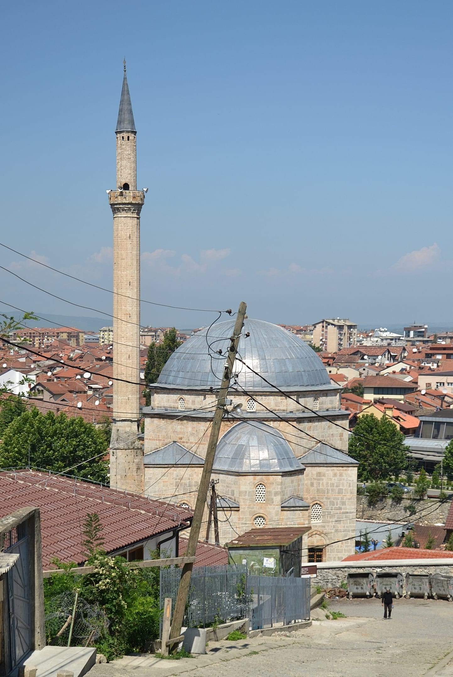 A large domed Ottoman mosque with a tall minaret rising above a river and old bridge