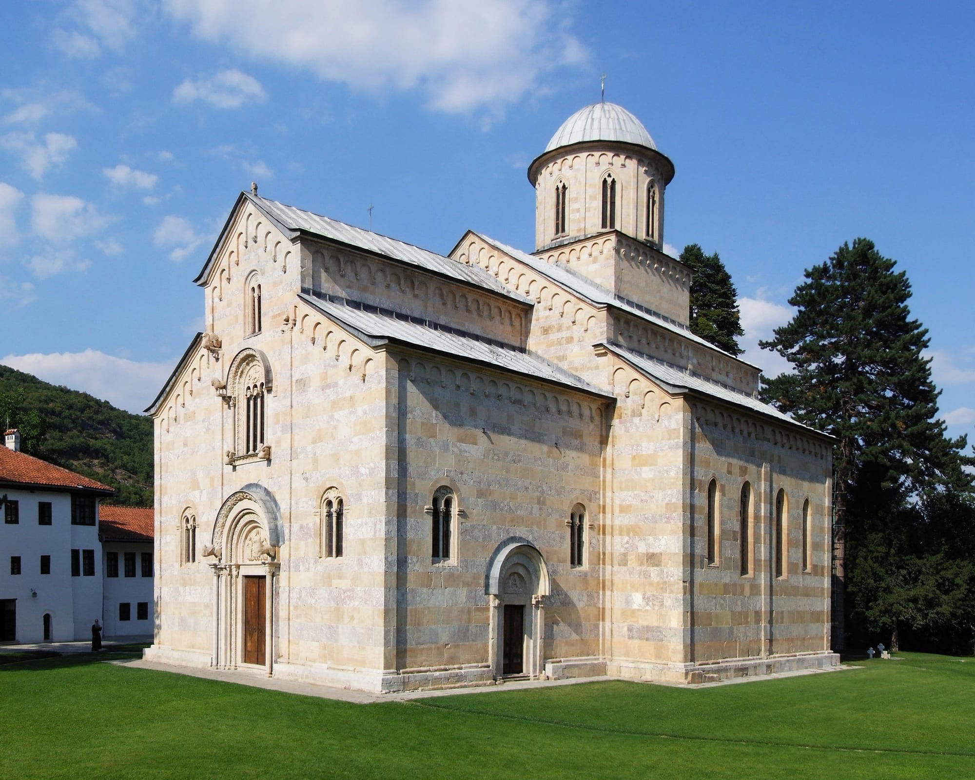 A striped marble medieval church with a tall dome, in a walled monastery courtyard