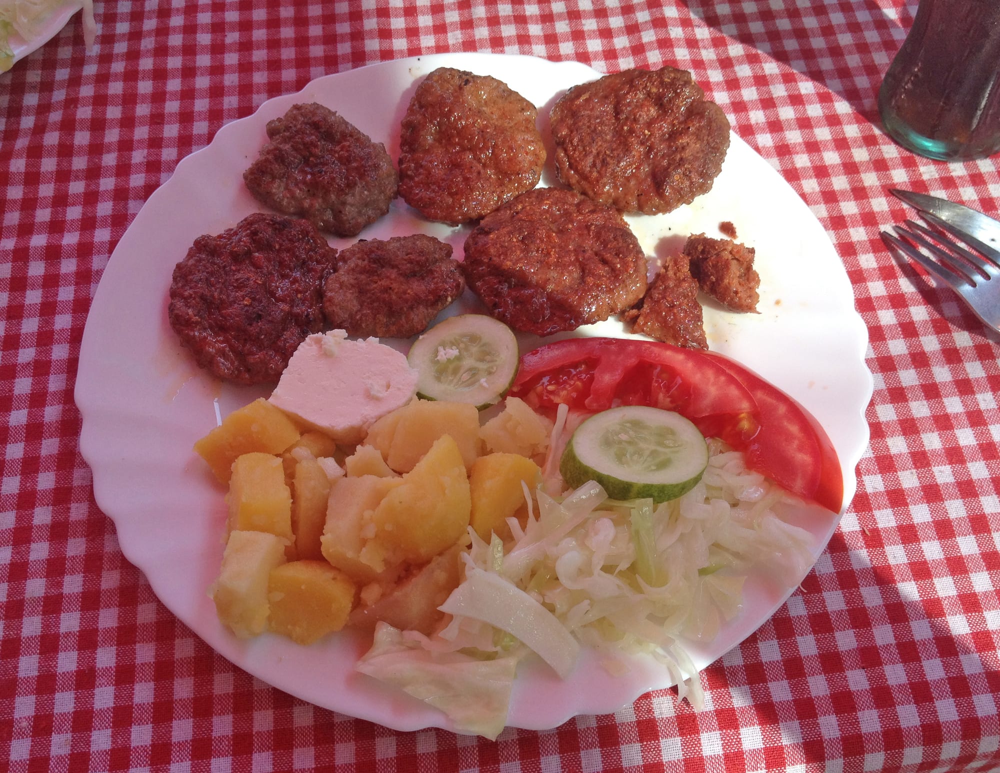 A plate of grilled minced-meat sausages served with cheese, potatoes and vegetables