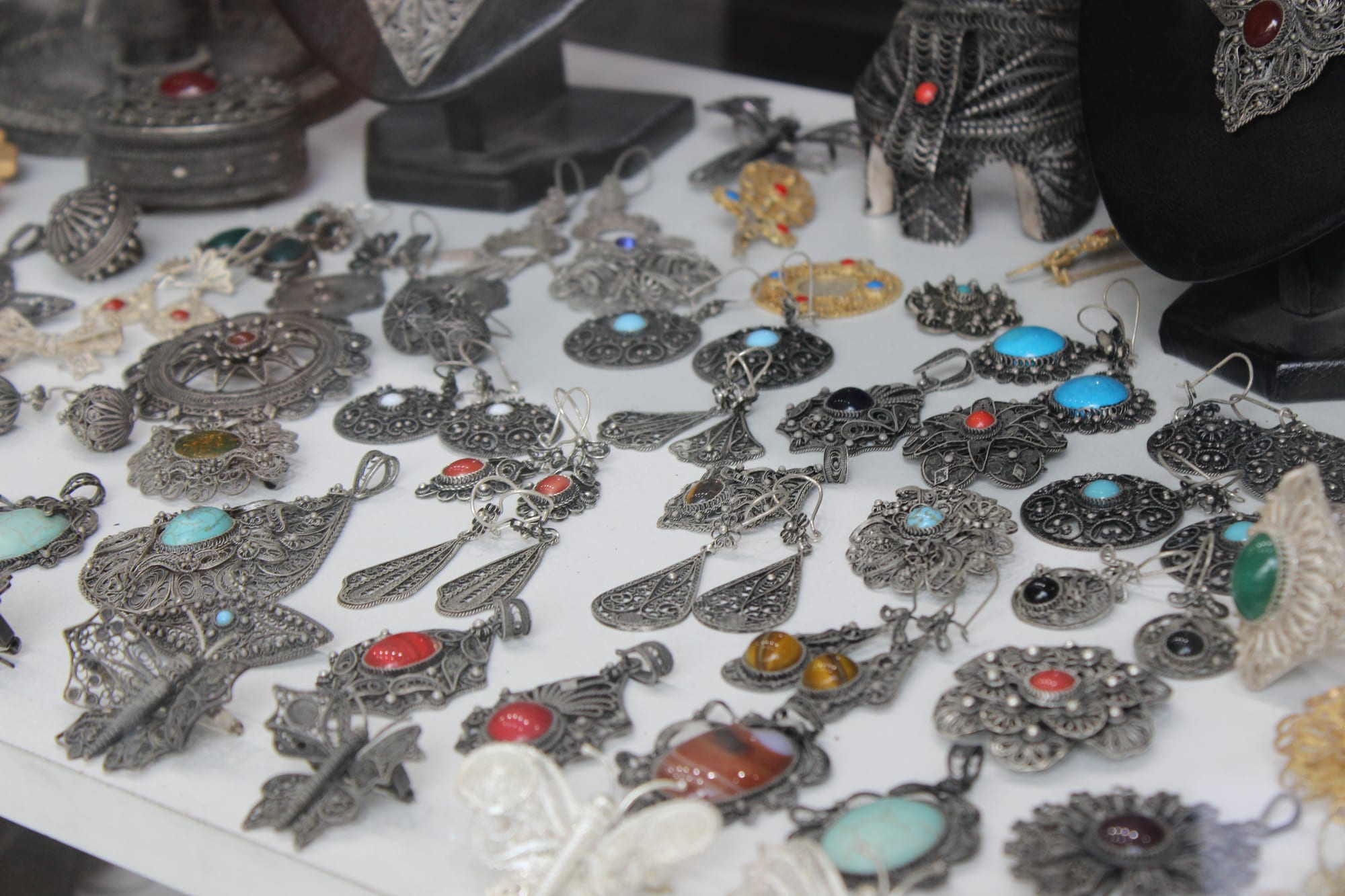 Rows of silver filigree earrings, pendants and brooches, many set with turquoise, red and green stones, laid out on a white display shelf